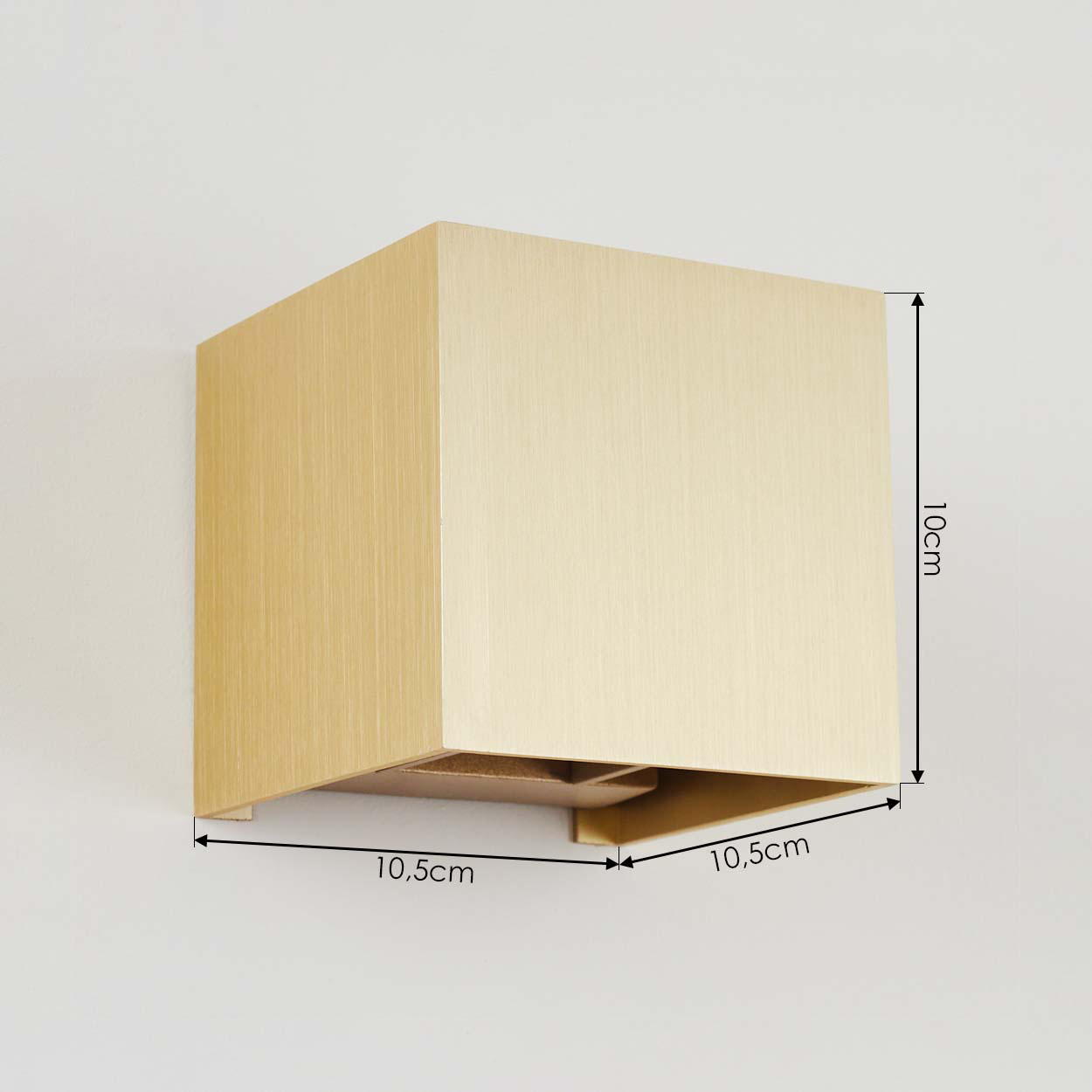 Eine goldene quadratische Wandleuchte an einer weißen Wand. Abmessungen: 10 cm Höhe, 10,5 cm Breite.