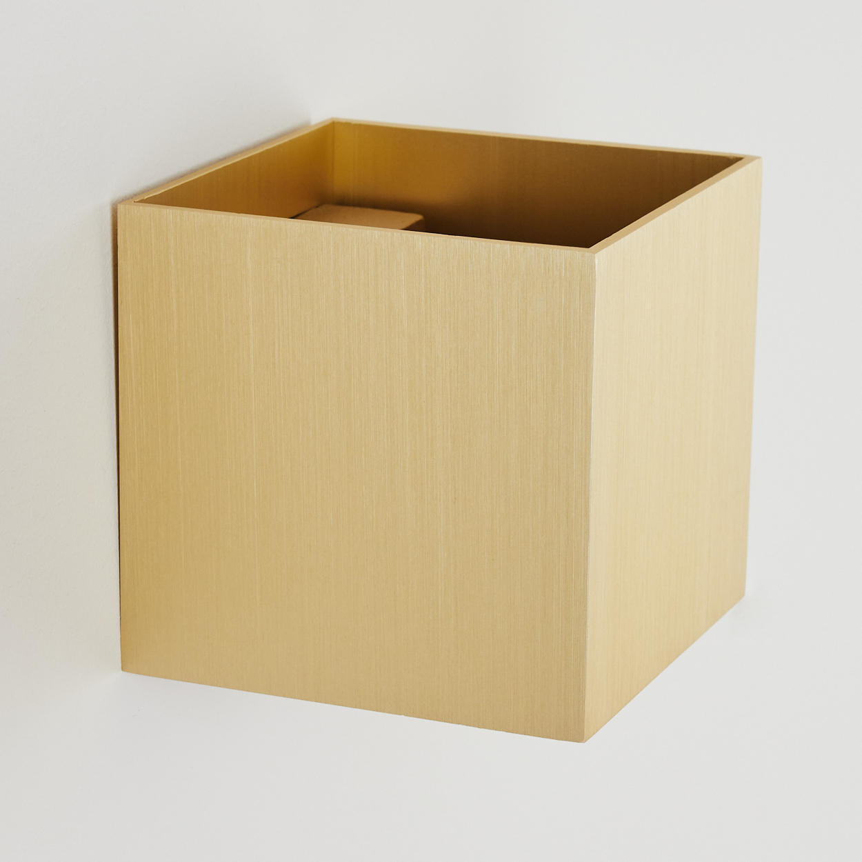 Eine goldfarbene quadratische Box, die an einer weißen Wand befestigt ist. Die Box ist oben offen.