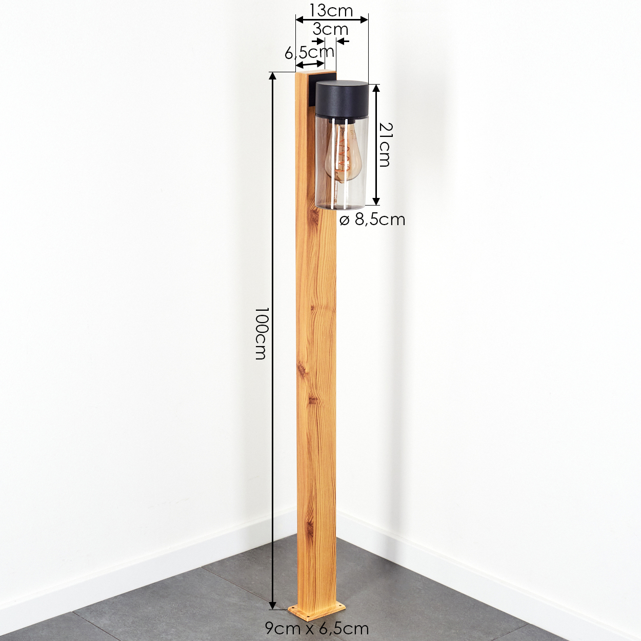 Holz-Außenlampe mit Maßen. Die Lampe hat einen schwarzen Deckel und einen Glaskörper. Der Sockel ist aus Holz, der Boden grau.