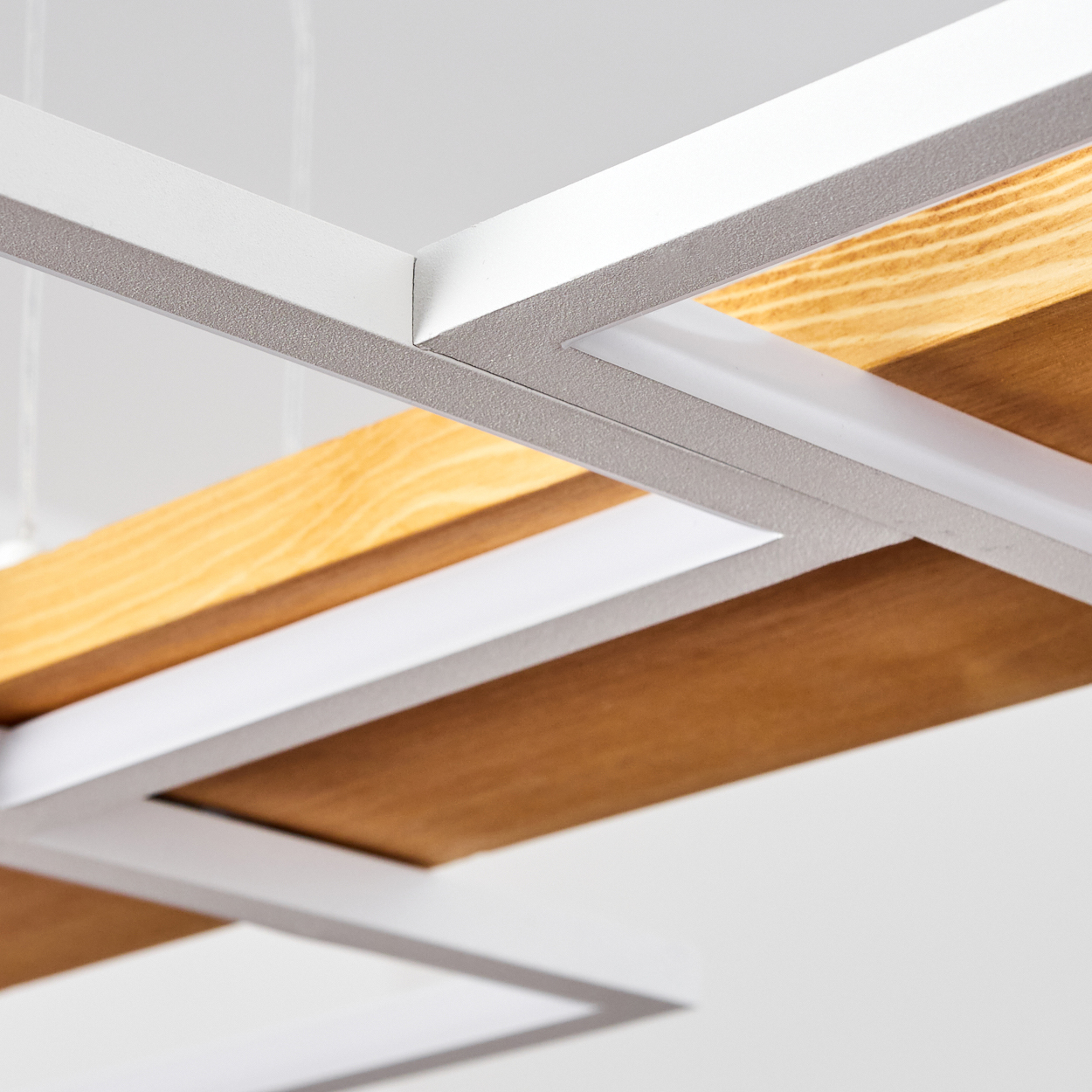 Nahaufnahme eines modernen Deckendesigns. Weiße Metallrahmen umgeben Holzpaneele in hellen und dunklen Brauntönen. Der Hintergrund ist weiß.