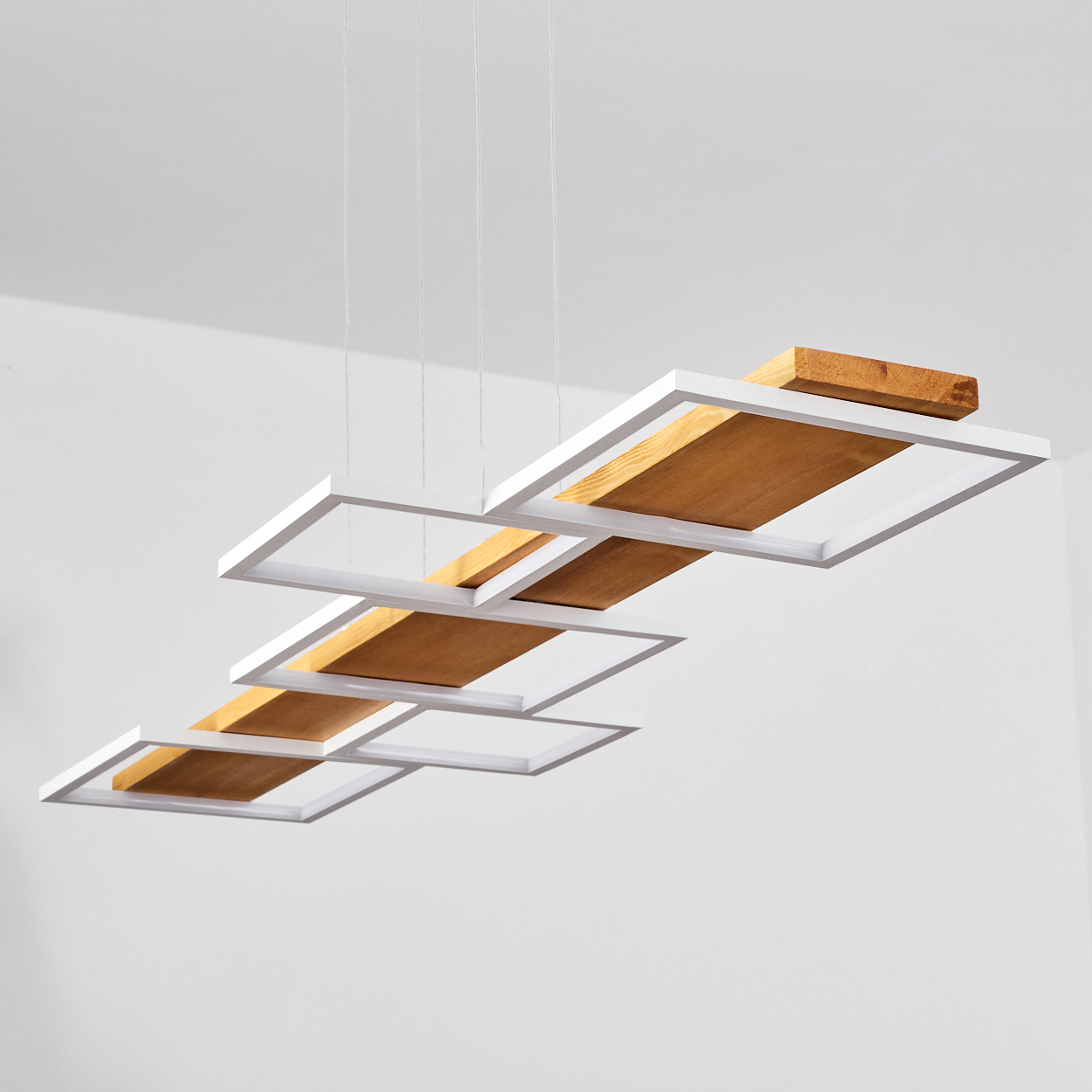 Moderne Deckenleuchte mit weißen Rahmen, Holzbrettern und weißer Decke. Die Leuchte wird von dünnen Drähten getragen.