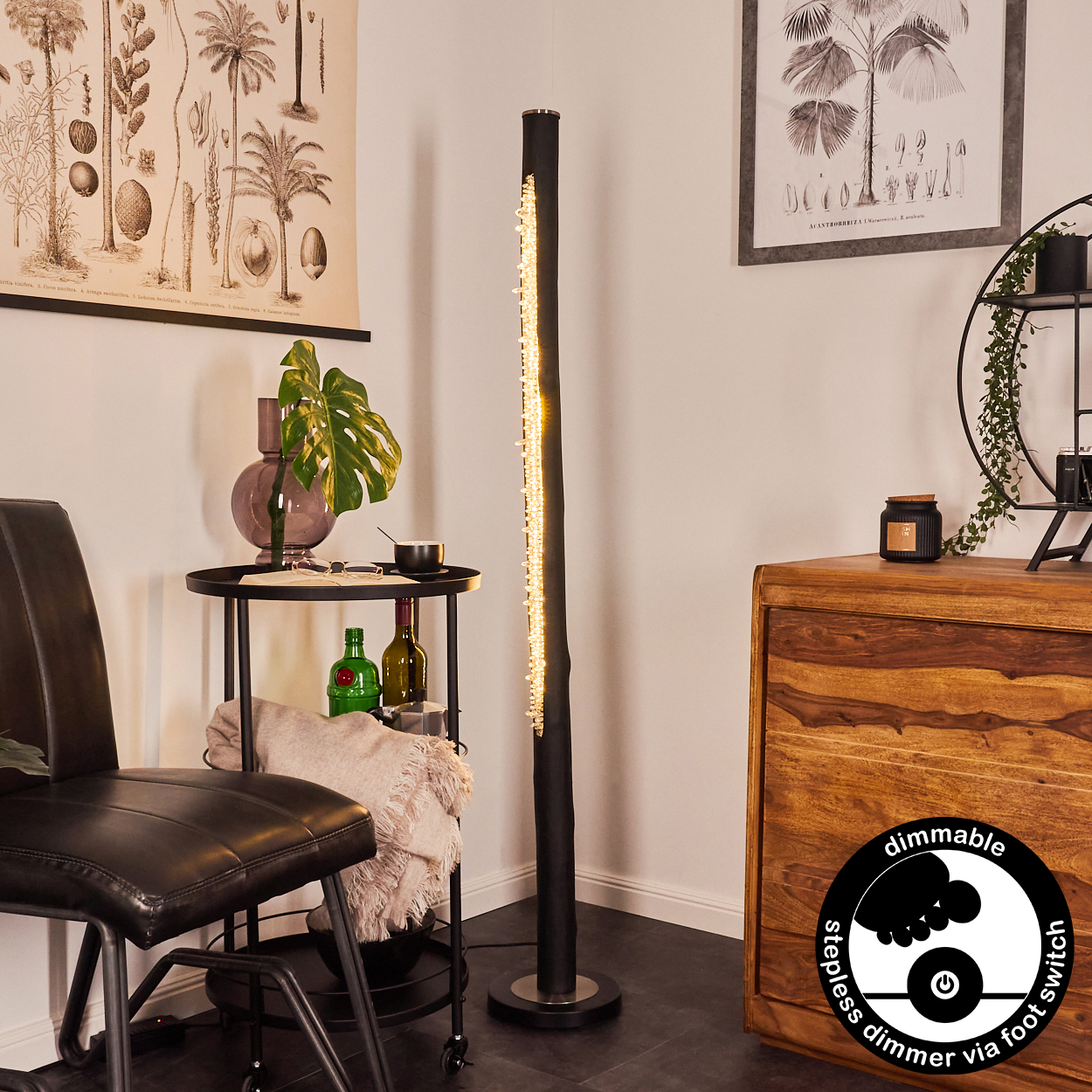 Ein Raum mit einer schwarzen Lampe, einem Beistelltisch mit Stuhl und einem Holzschrank. Botanische Kunst ziert die Wände.