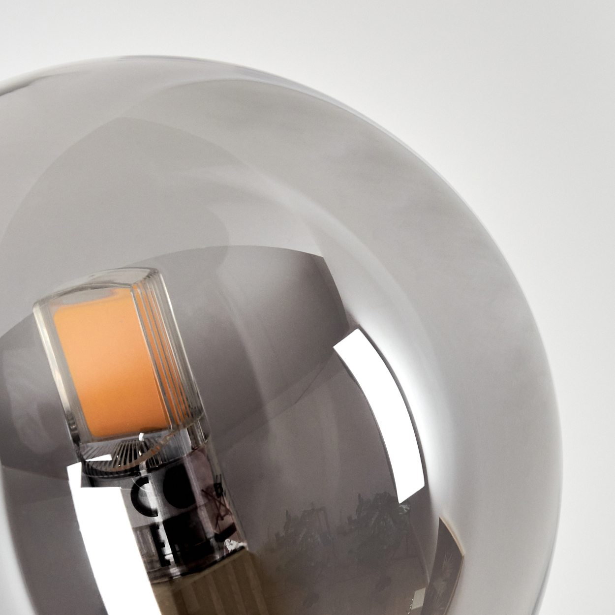 Nahaufnahme einer Glühbirne mit rauchigem Glas. Das Innere der Birne ist sichtbar und zeigt eine orangefarbene Lichtquelle vor weißem Hintergrund.