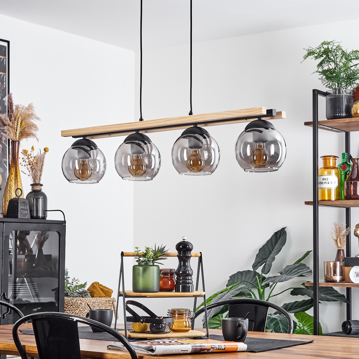 Ein Esszimmer mit Holztisch, schwarzen Stühlen und einer Hängeleuchte. Pflanzen und Dekorationen befinden sich auf Regalen und Tisch.