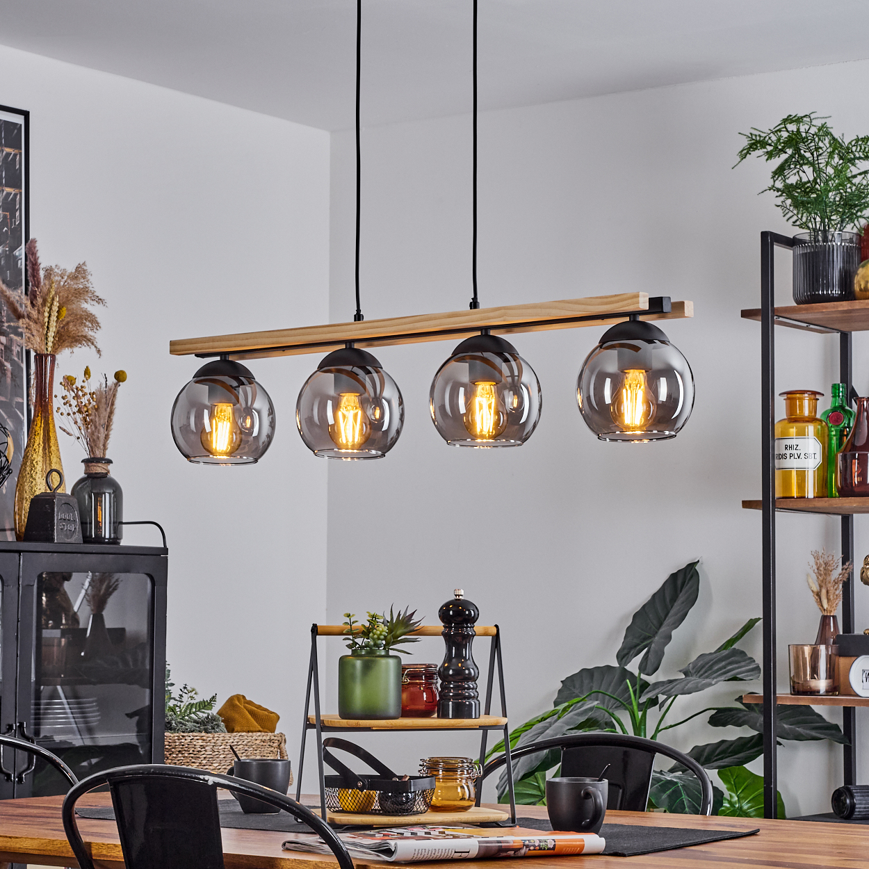 Esszimmer mit Hängelampen, Holztisch, schwarzen Stühlen und Regalen mit Pflanzen und Dekorationen.