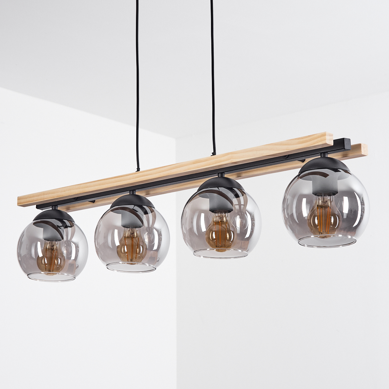 Eine moderne Leuchte mit vier Glaskugelschirmen, Holzbalken und schwarzen Akzenten, die an der Decke vor einer weißen Wand hängt.