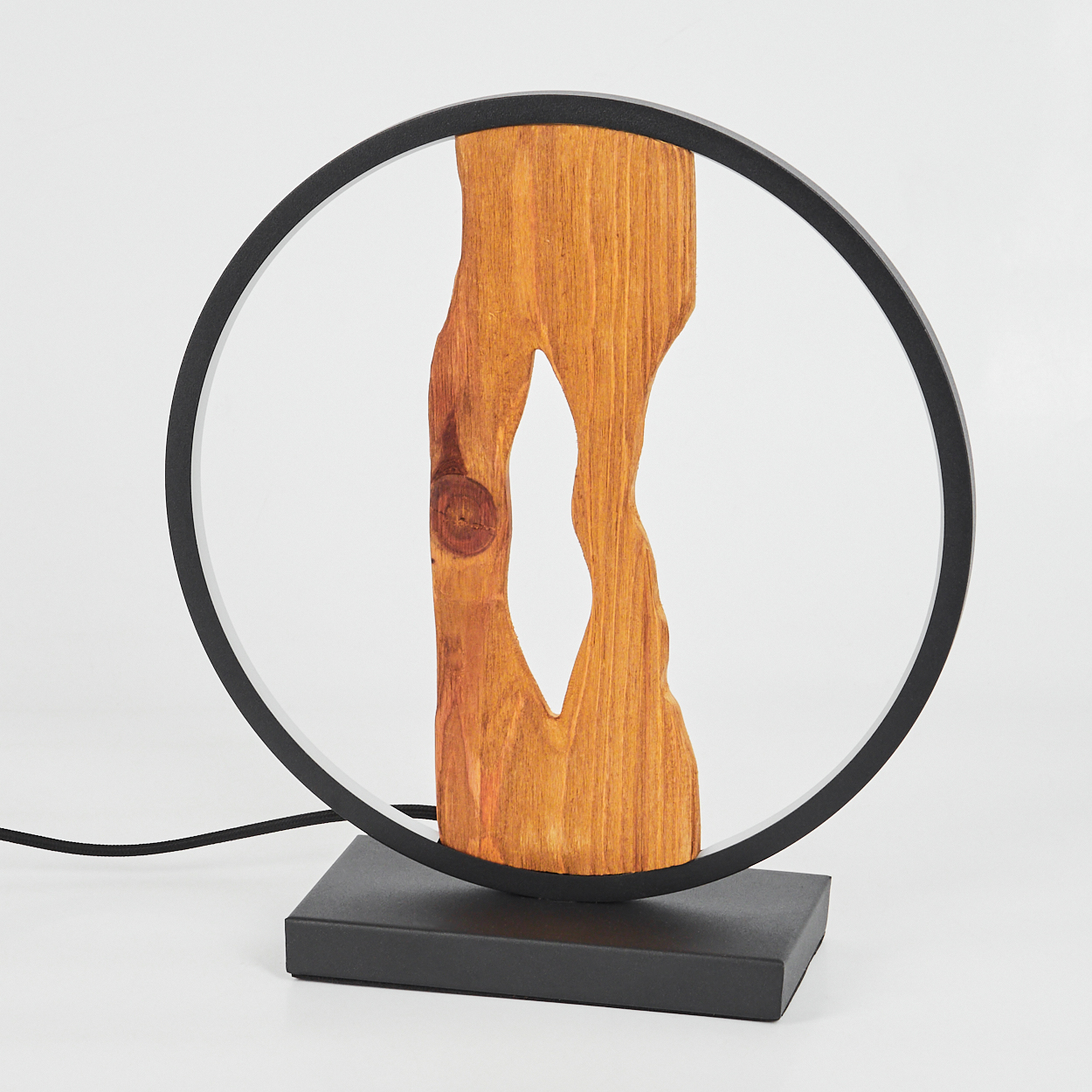 Eine moderne Lampe mit einem Holzmittelstück und einem schwarzen kreisförmigen Rahmen. Sie steht auf einem schwarzen Sockel. Der Hintergrund ist weiß.