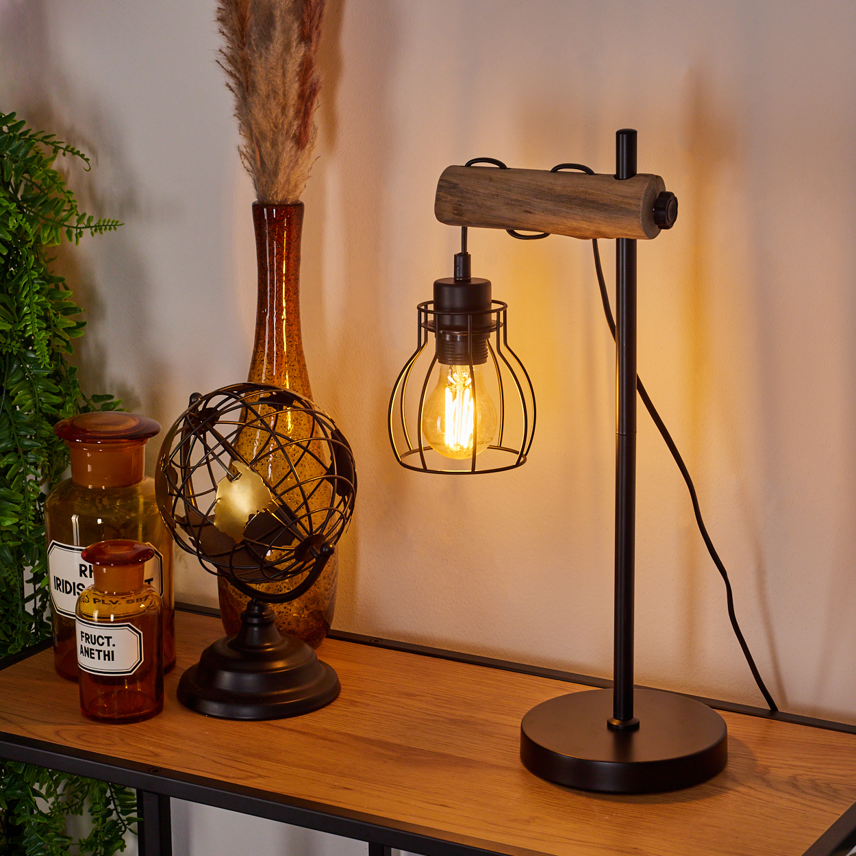 Ein Holztisch mit einer Lampe, einem Globus und dekorativen Vasen. Die Lampe hat einen Käfigschirm. Trockenpflanzen in einer Vase.