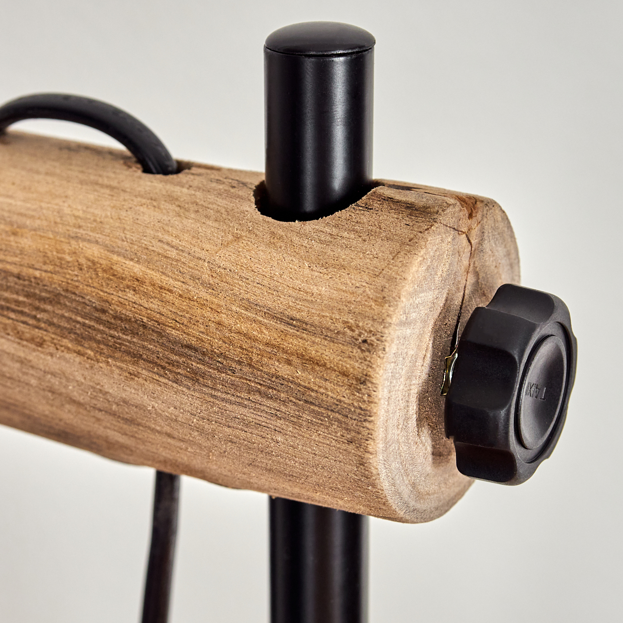 Nahaufnahme eines Holzblocks mit schwarzem Griff und schwarzem Knopf. Schwarze Metallbeine und ein schwarzer Zylinder sind ebenfalls sichtbar.