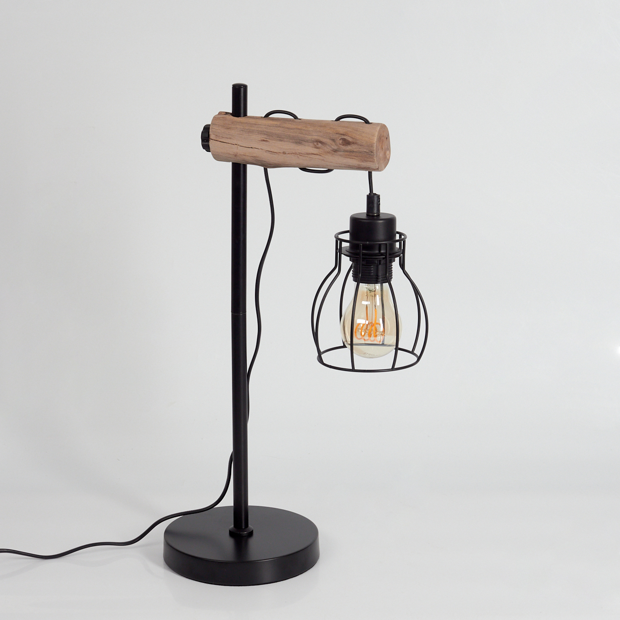 Eine schwarze Metall-Schreibtischlampe mit Holzbalken, Drahtkäfig-Glühbirne und rundem Sockel. Der Hintergrund ist weiß.