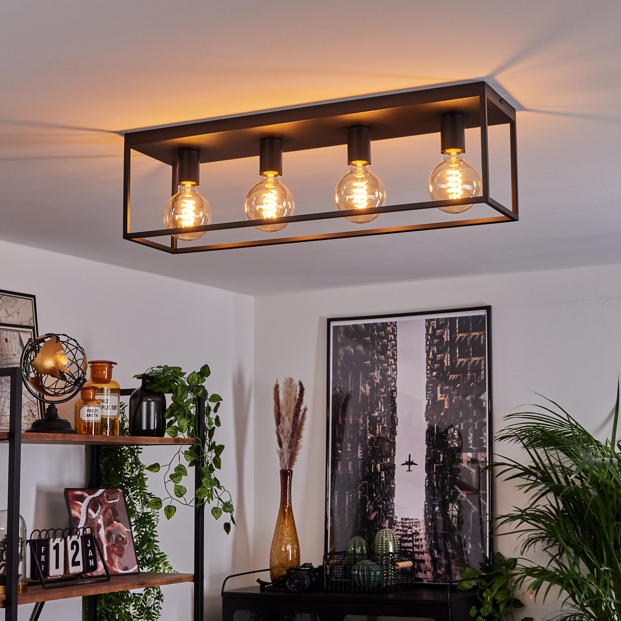 Eine rechteckige schwarze Deckenlampe mit vier runden Glühbirnen. Regale mit Dekor und ein Stadtbild im Hintergrund.