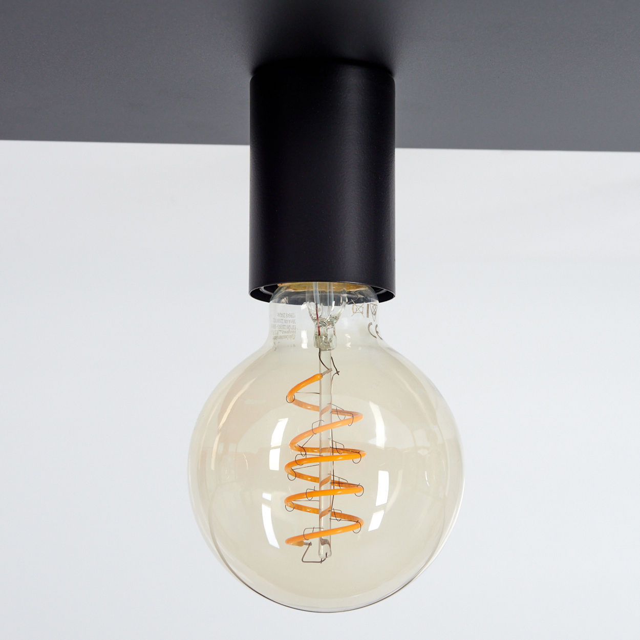 Schwarze Deckenlampe mit großer, runder Glühbirne. Die Birne hat einen orangefarbenen Wendel. Weißer Hintergrund.