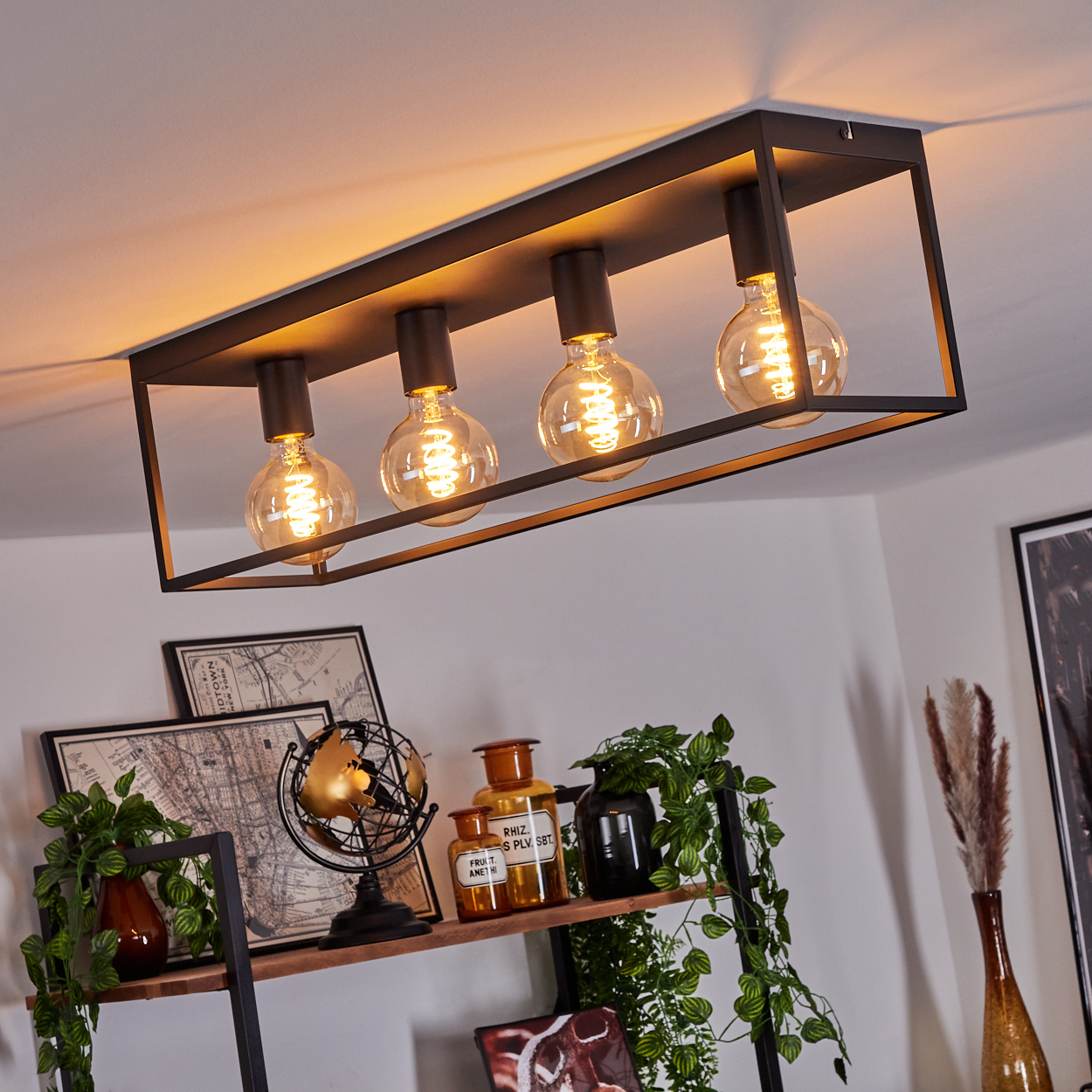 Eine moderne Deckenlampe mit vier Edison-Glühbirnen hängt über einem Regal mit Dekoration. Das Regal hat Pflanzen, Globus und Flaschen.