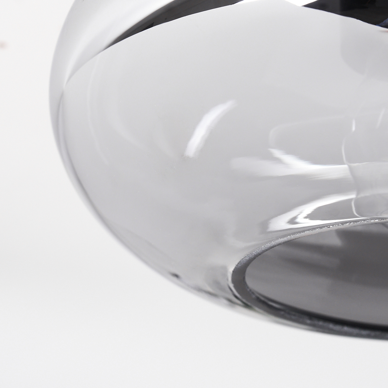 Nahaufnahme eines transparenten, grauen, kugelförmigen Glasobjekts vor weißem Hintergrund. Das Objekt reflektiert Licht.