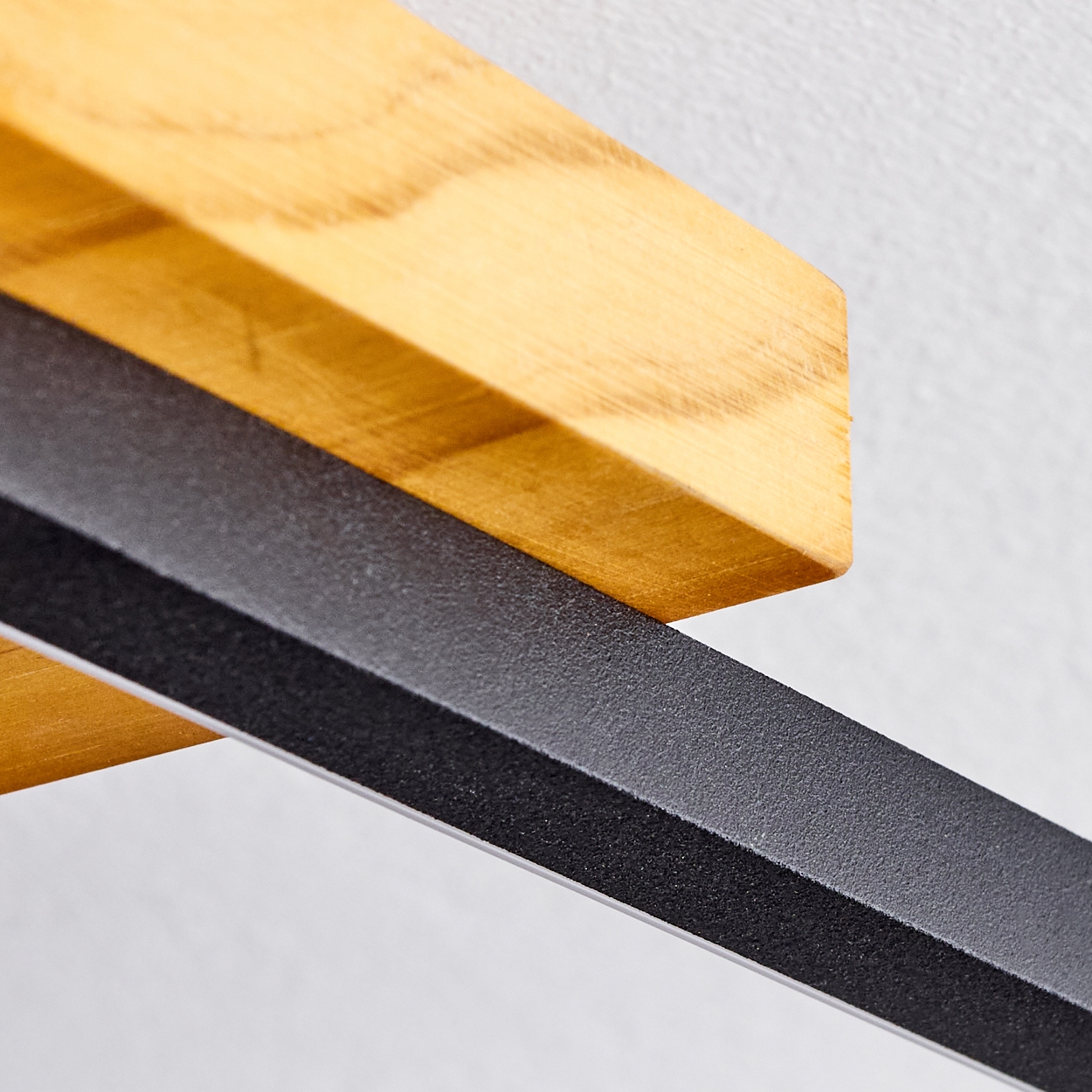 Nahaufnahme eines Holzregals und einer schwarzen Metallhalterung. Das Regal ist hellbraun, die Halterung ist schwarz und strukturiert, vor einer weißen Wand.