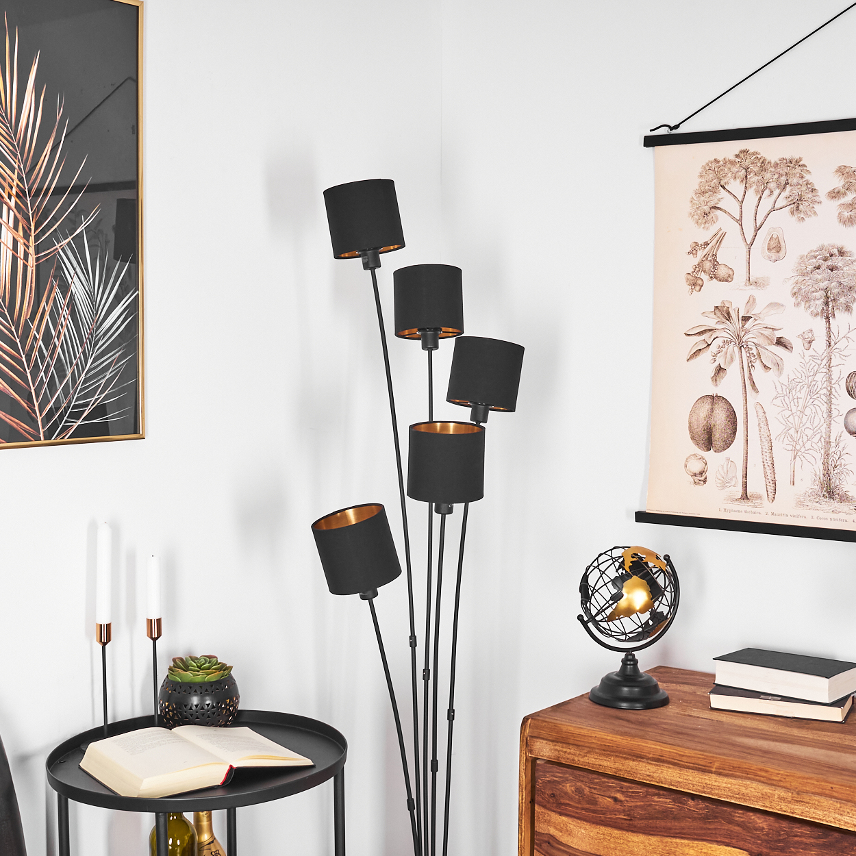 Eine Zimmerecke mit Stehlampe, Gemälden und einem Beistelltisch mit Dekoration. Schwarze Lampenschirme mit Gold innen. Holzschrank.