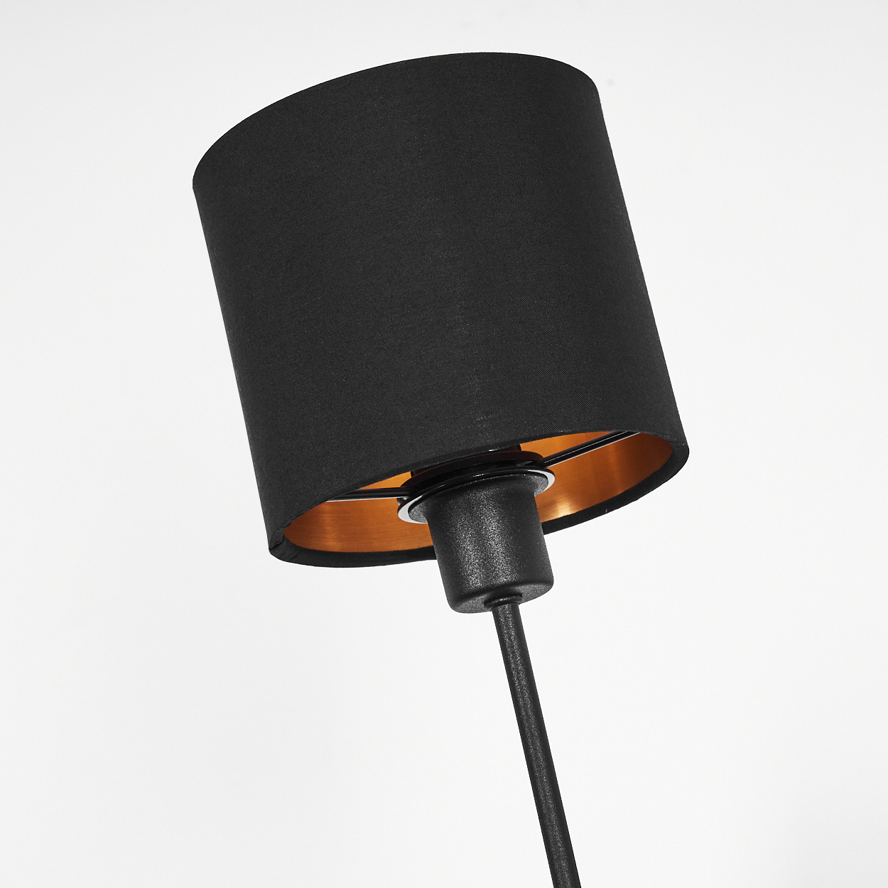 Ein schwarzer Lampenschirm mit goldenem Innenraum ist geneigt. Die Lampe hat einen schwarzen Stiel, vor weißem Hintergrund.
