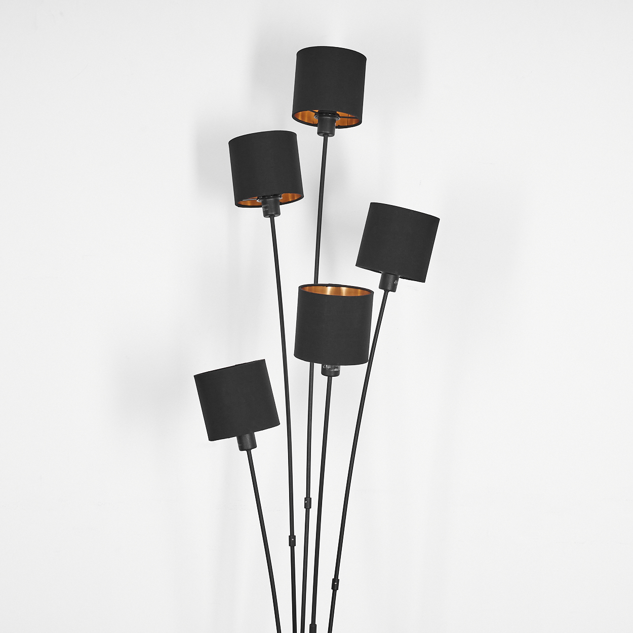 Eine schwarze Stehlampe mit fünf Schirmen. Die Schirme sind zylindrisch und innen goldfarben. Der Hintergrund ist eine weiße Wand.