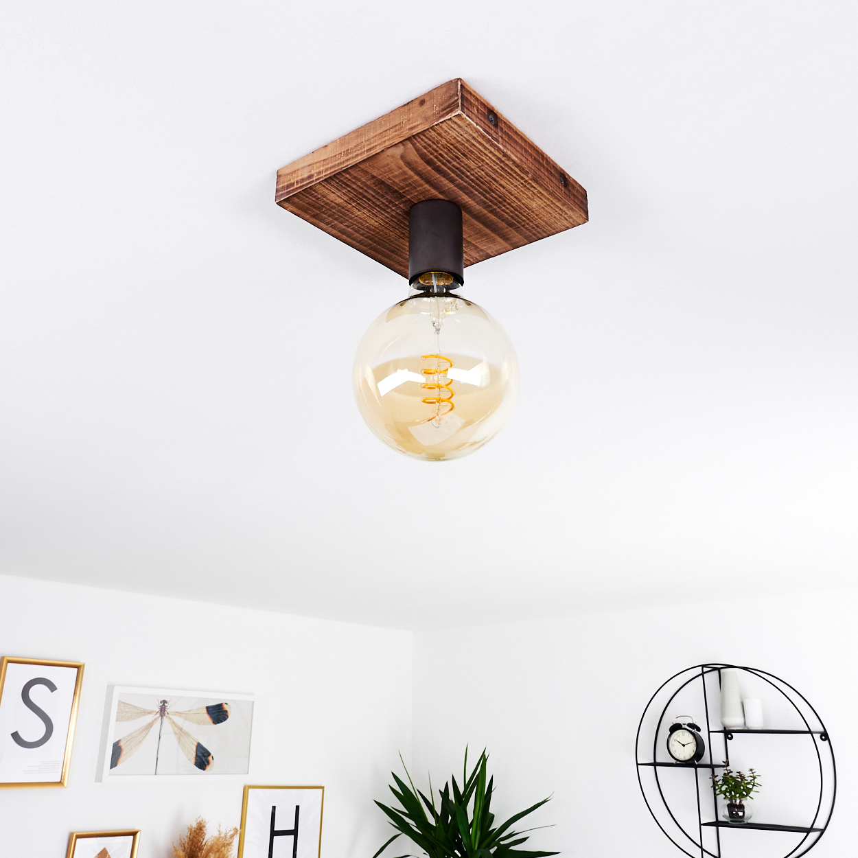 Eine Deckenlampe aus Holz mit großer Glühbirne. Der Raum hat weiße Wände, Kunstwerke und ein schwarzes Regal.