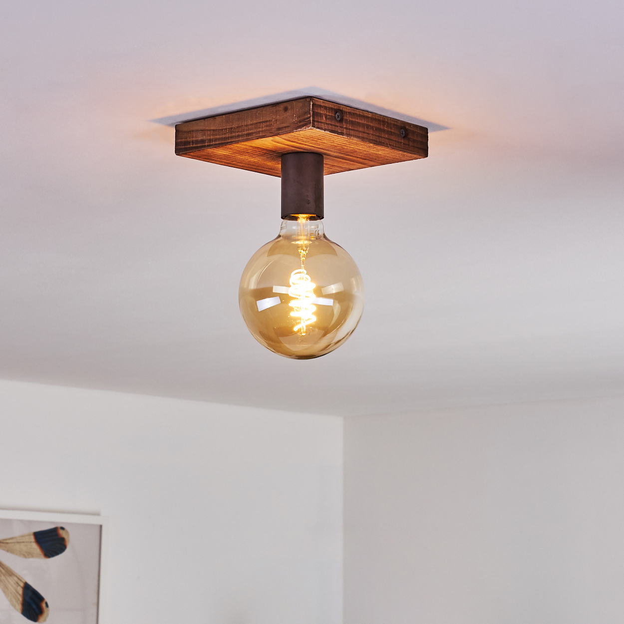 Eine Deckenleuchte mit quadratischer Holzbasis und einer runden, warm getönten Glühbirne. Das Licht hängt an einem dunklen Metallzylinder.