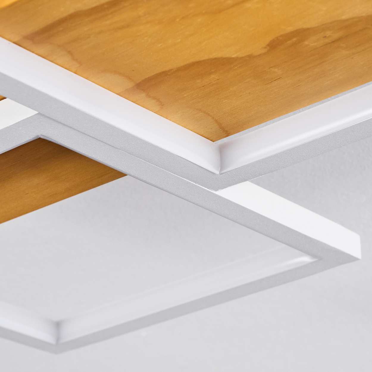 Nahaufnahme einer Deckenstruktur. Holzpaneele werden von weißen, geometrischen Formen umrahmt. Der Hintergrund ist eine weiße Decke.