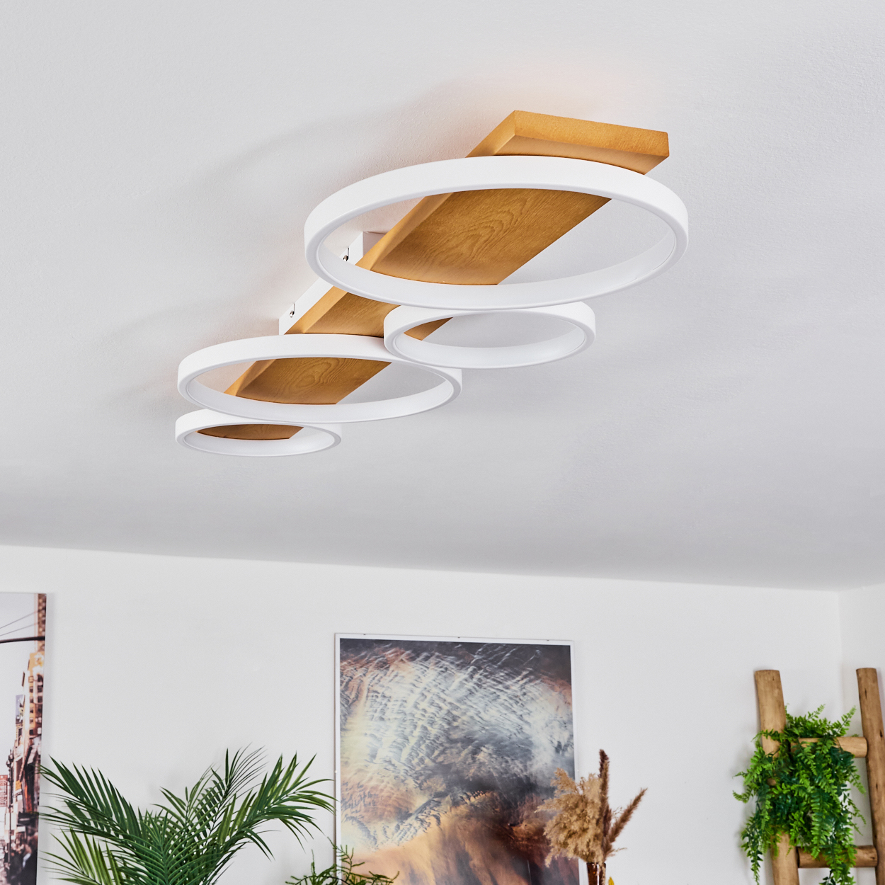 Deckenleuchte mit weißen kreisförmigen Lichtern, braunen Holzakzenten. Pflanzen und Kunstwerke sind im Hintergrund sichtbar.