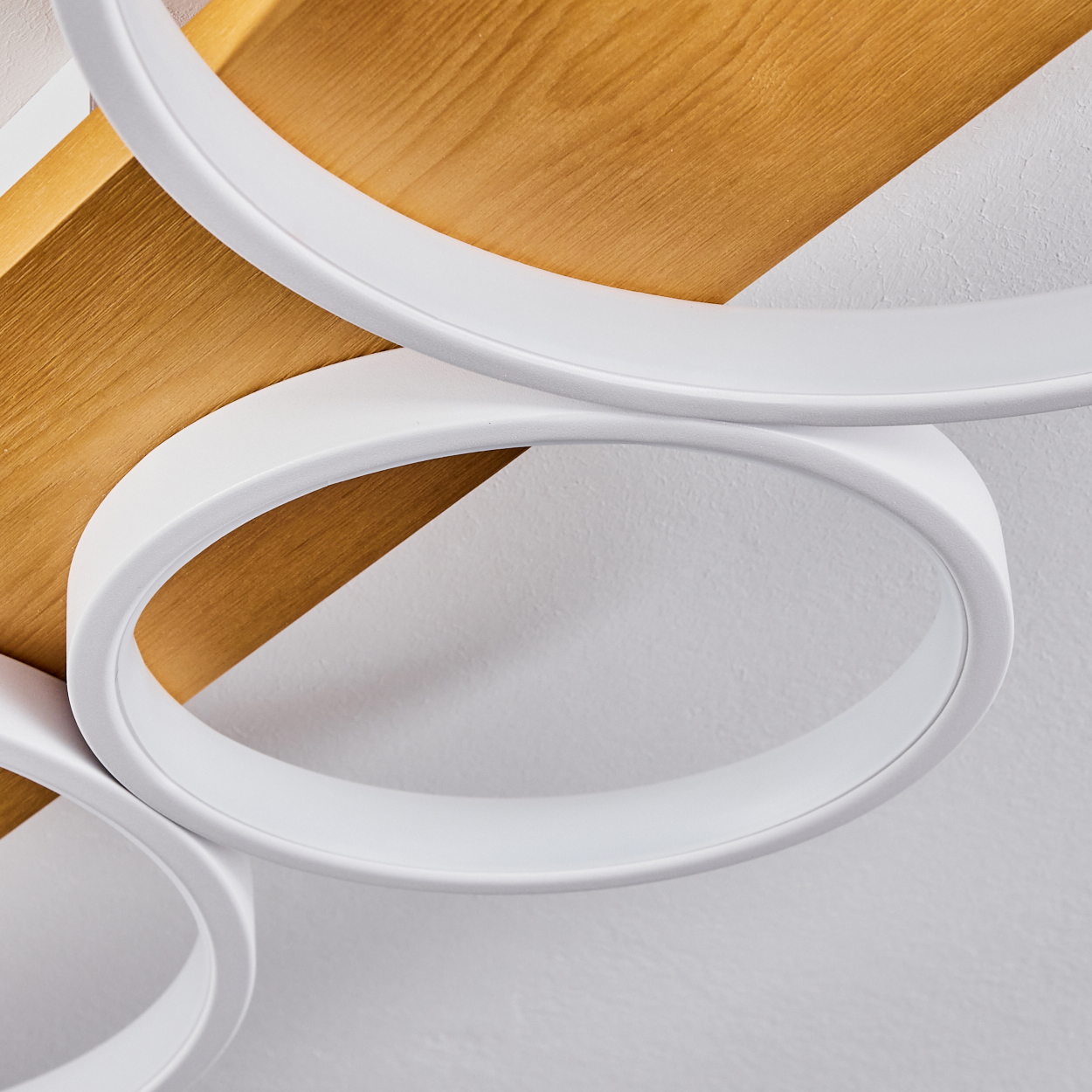 Nahaufnahme einer weißen, kreisförmigen Leuchte vor einer Holzplatte und weißer Wand. Die Leuchte hat ein glattes, modernes Design.