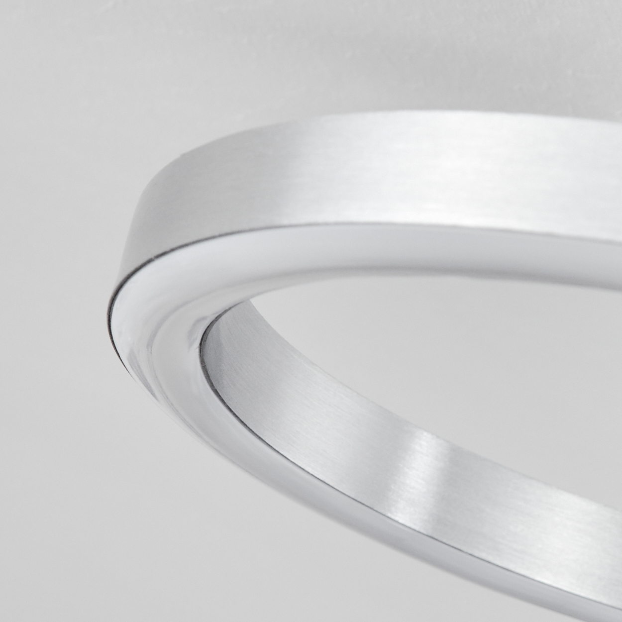 Nahaufnahme eines gebürsteten Metallrings, gebogen. Der Hintergrund ist ein schlichtes, helles Grau. Der Ring ist glänzend und reflektierend.