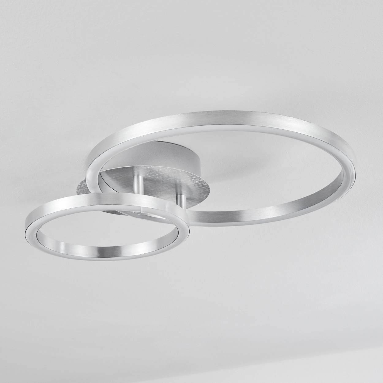 Eine moderne Deckenleuchte mit zwei silbernen Ringen, die sich überlappen. Der Hintergrund ist eine weiße Decke.