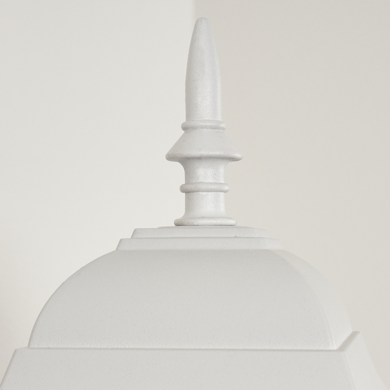 Nahaufnahme eines weißen, verzierten architektonischen Elements. Es hat eine spitze Spitze und eine abgerundete, kuppelförmige Basis.