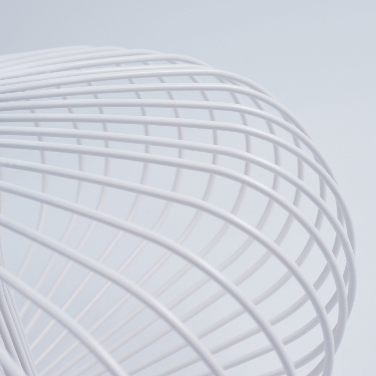 Nahaufnahme einer weißen, gebogenen Drahtstruktur vor weißem Hintergrund, die einem Käfig oder architektonischen Detail ähnelt.