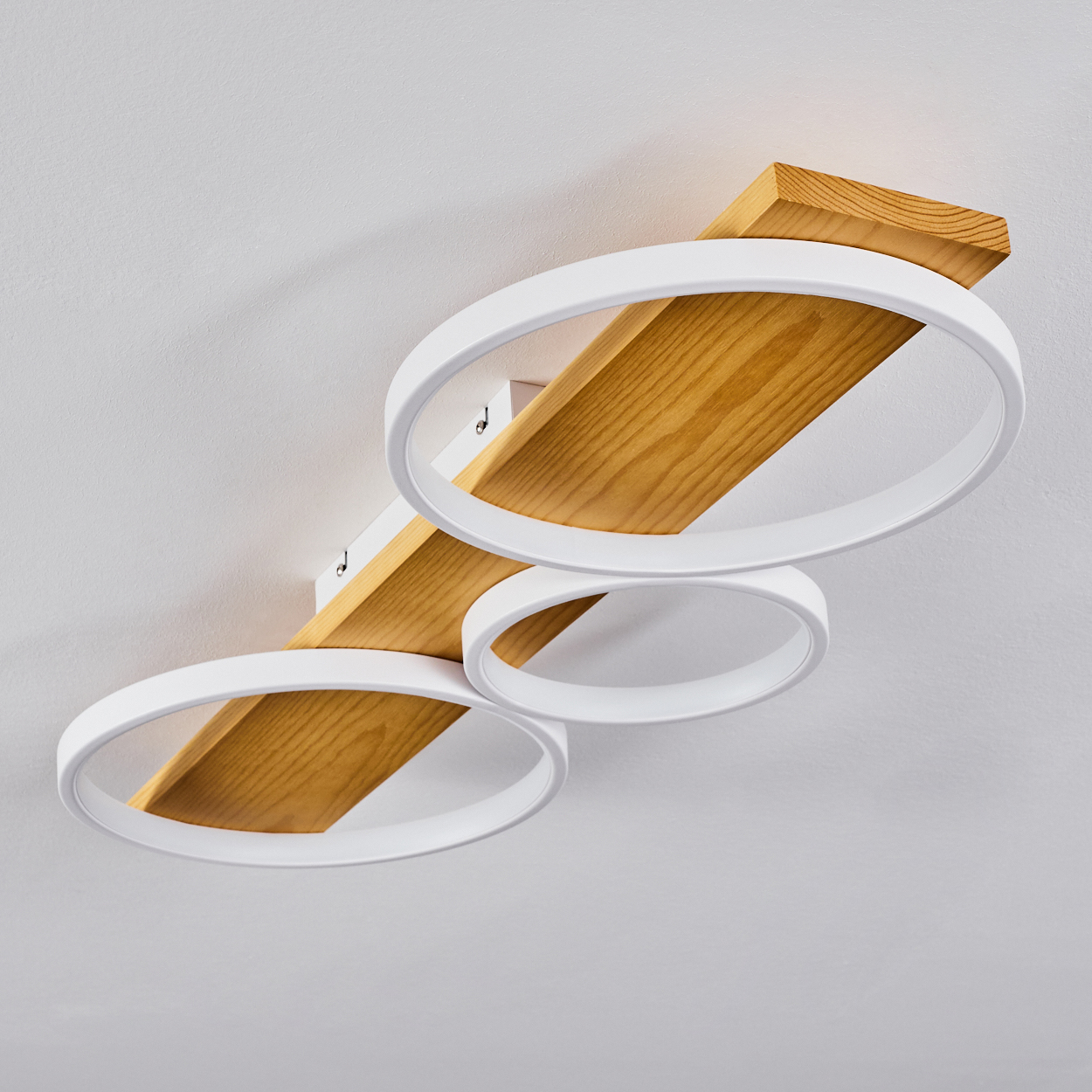 Eine Deckenleuchte. Sie hat drei weiße kreisförmige Lichter, die an einem Holzbrett an einer weißen Decke befestigt sind.