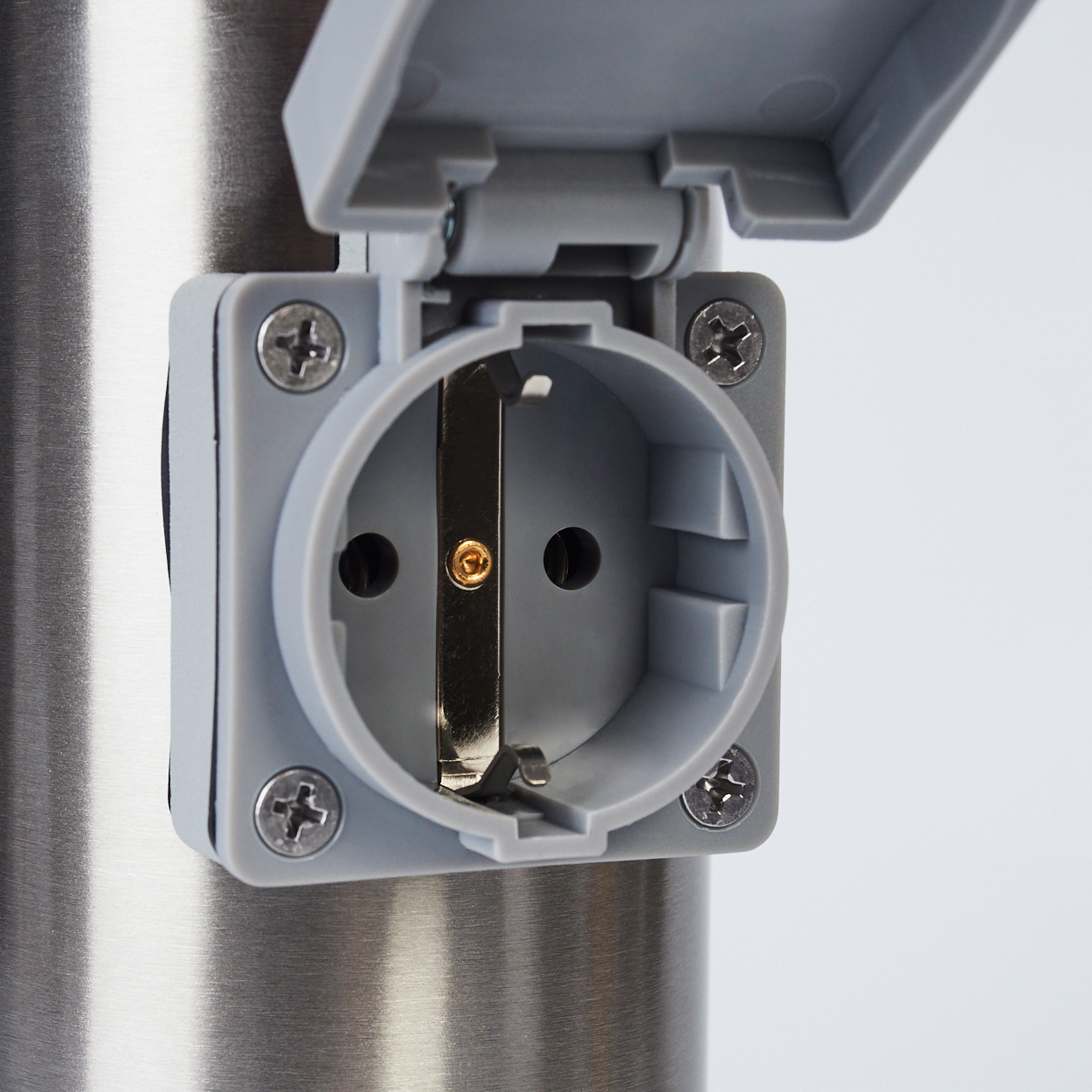 Eine graue Steckdose mit offenem Deckel ist an einer Metallsäule befestigt. Schrauben sichern die Abdeckung und die Steckdose selbst.