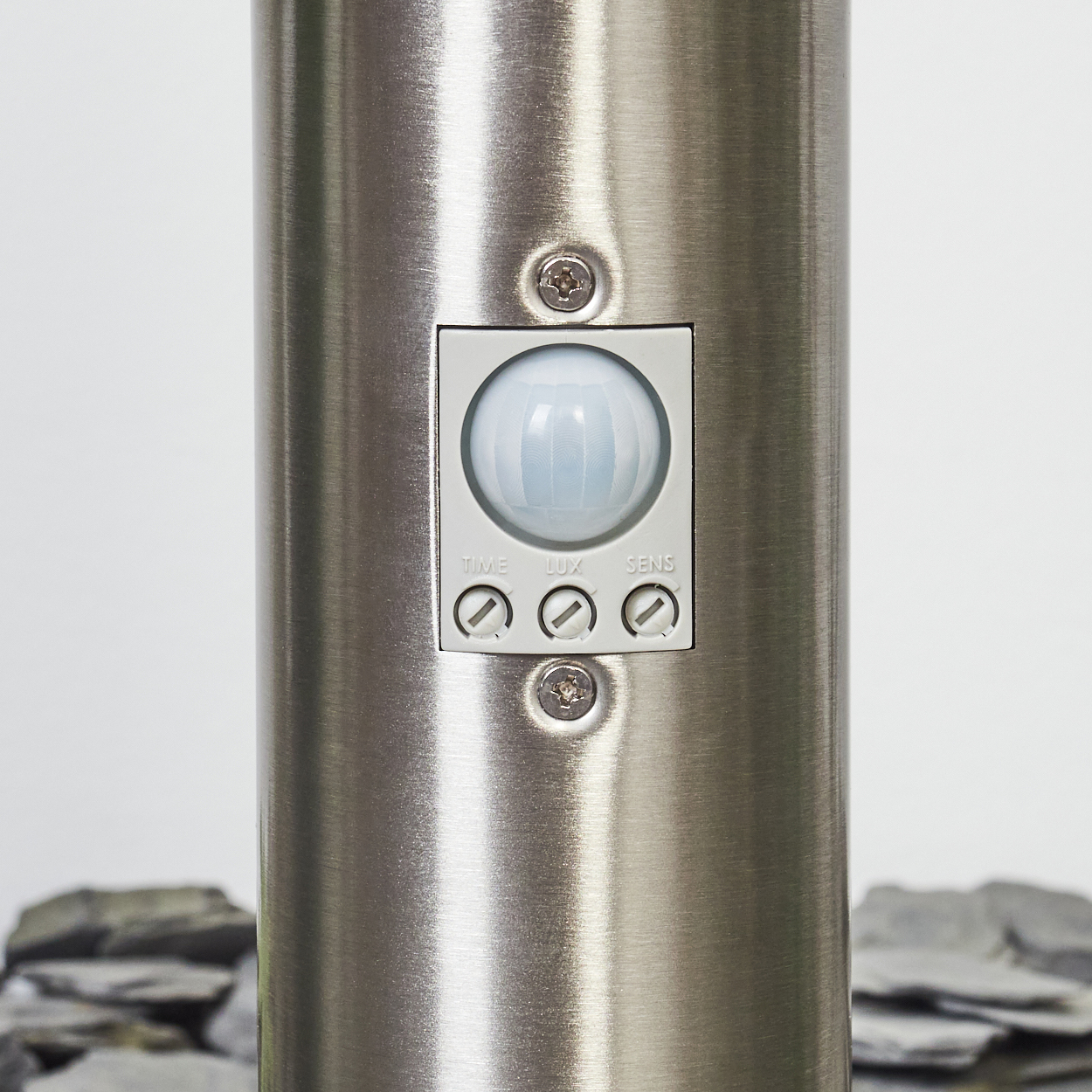 Eine Edelstahlstange mit Sensoreinheit. Der Sensor hat eine Linse und Einstellungen für Zeit, Lux und Empfindlichkeit. Graue Steine befinden sich am Sockel.