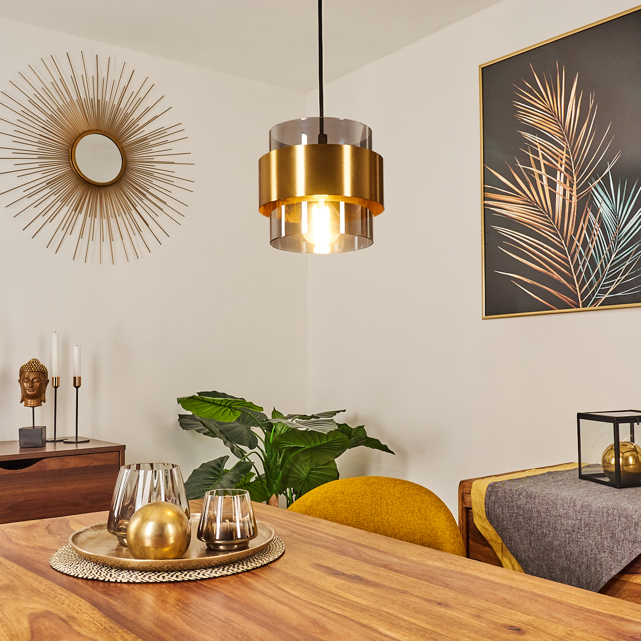 Ein Esszimmer mit Holztisch, goldenen Akzenten, Hängelampe, Gemälde, Pflanzen und gelbem Stuhl.