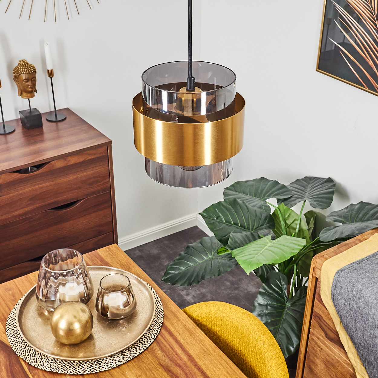 Ein modernes Interieur mit einer goldenen Lampe, einer Pflanze und Holzmöbeln. Ein Tablett mit Kerzen steht auf einem Tisch. Buddha-Statue links.