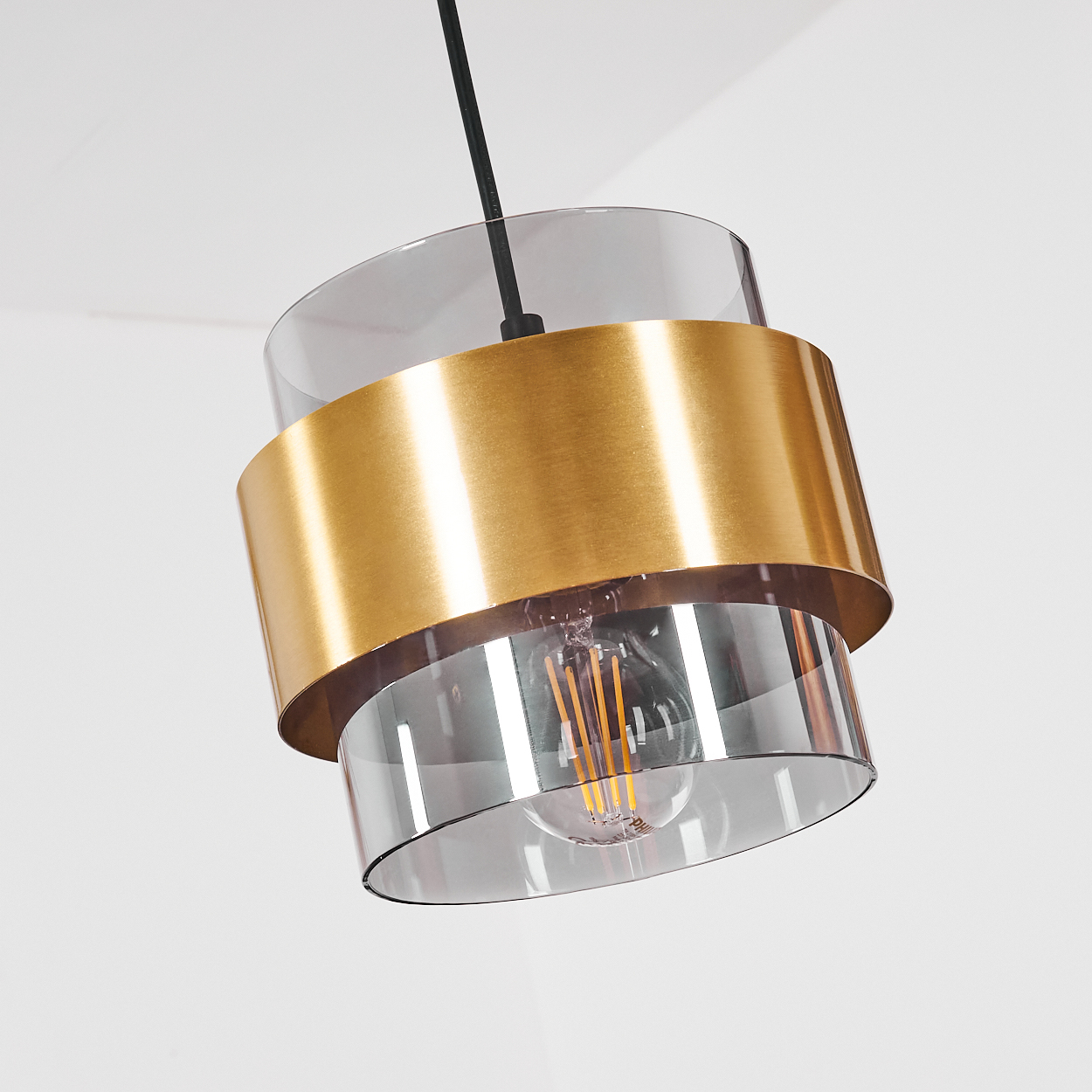 Eine moderne Pendelleuchte mit goldenem Band, Glas und sichtbarer Glühbirne. Der Hintergrund ist schlicht weiß.