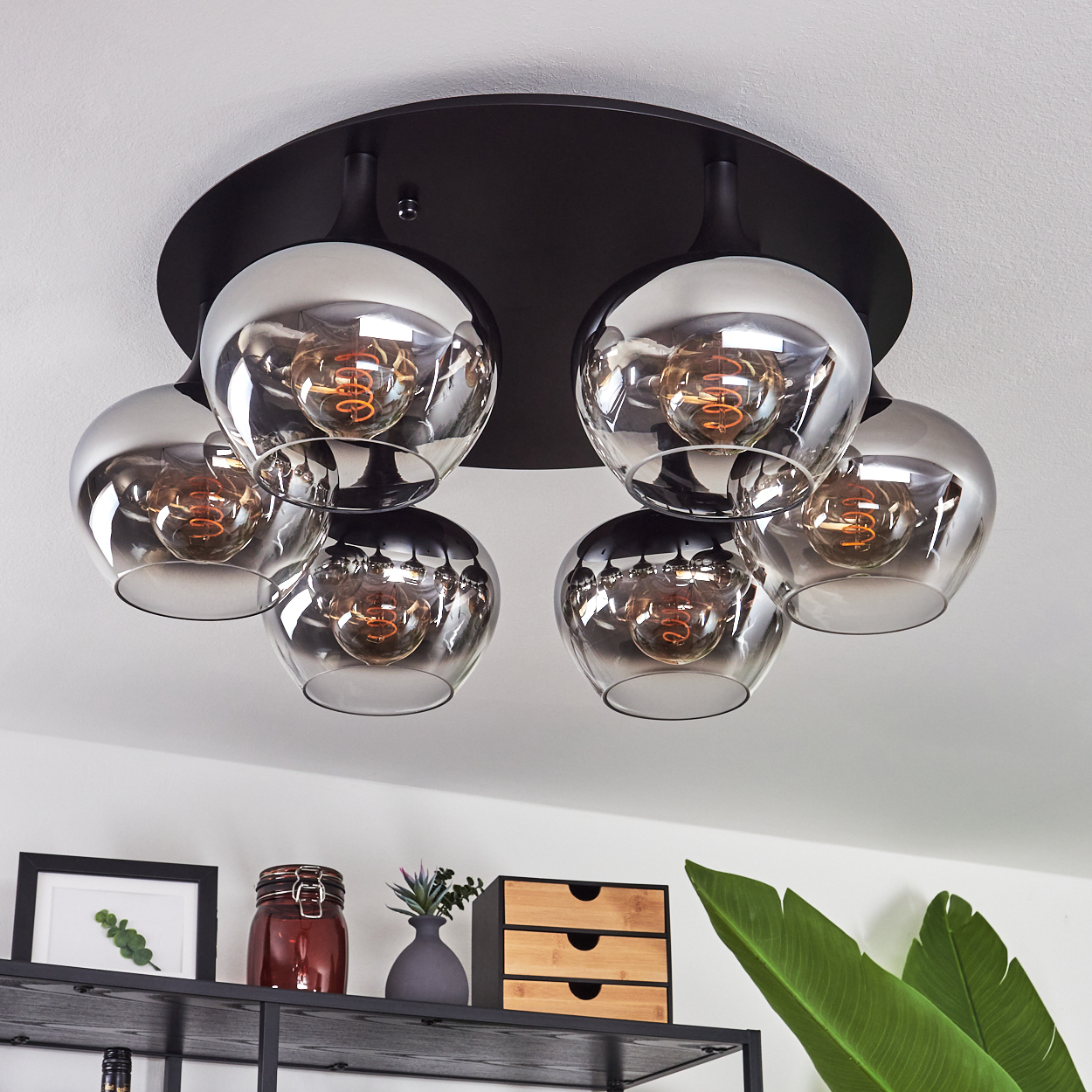 Eine moderne Deckenleuchte mit sechs kugelförmigen Glasschirmen, die jeweils eine sichtbare Glühbirne beherbergen, hängt über einem Regal mit Dekoration.