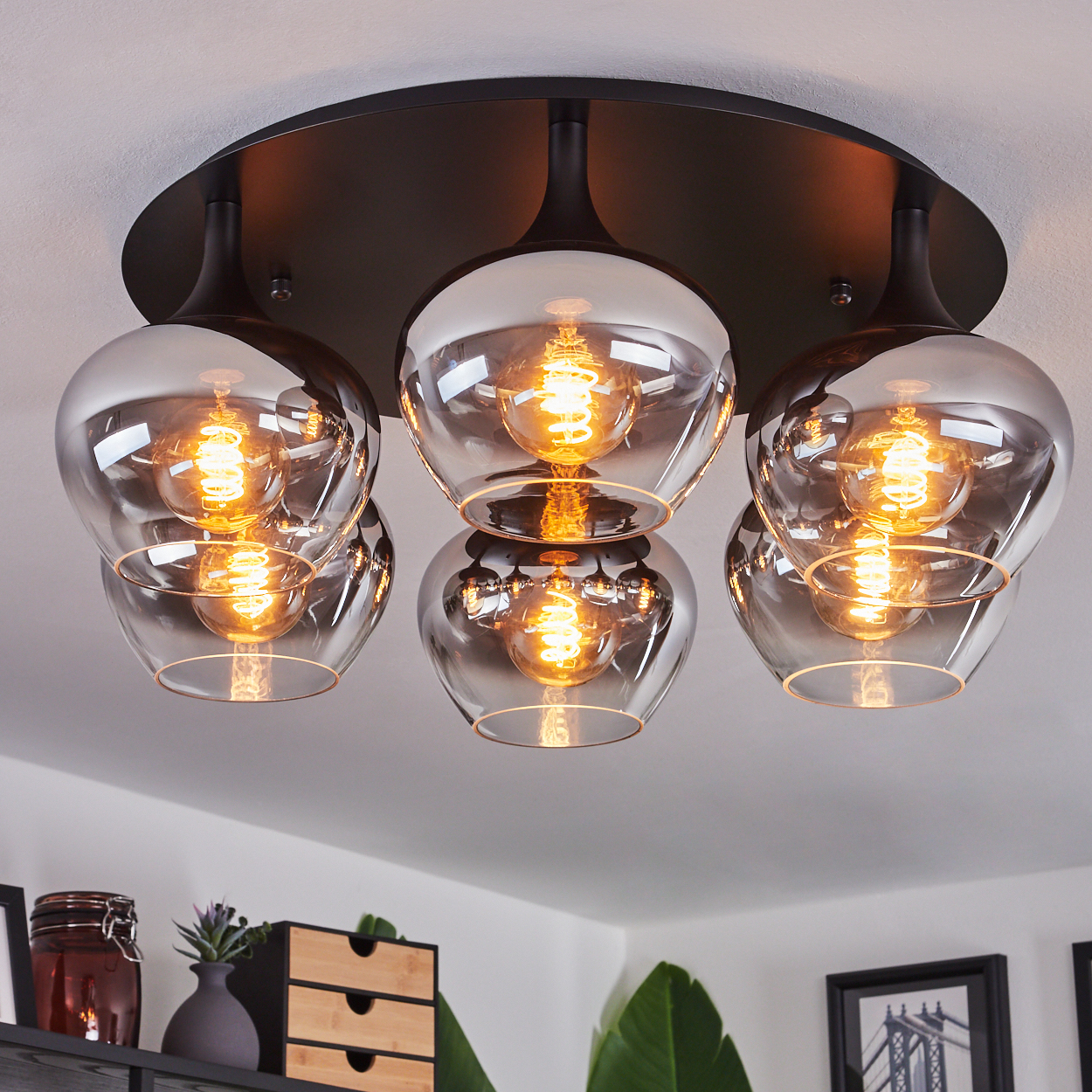 Eine moderne Deckenlampe mit fünf Glasschirmen, die jeweils eine helle, warme Glühbirne enthalten. Die Leuchte ist schwarz und an einer weißen Decke montiert.