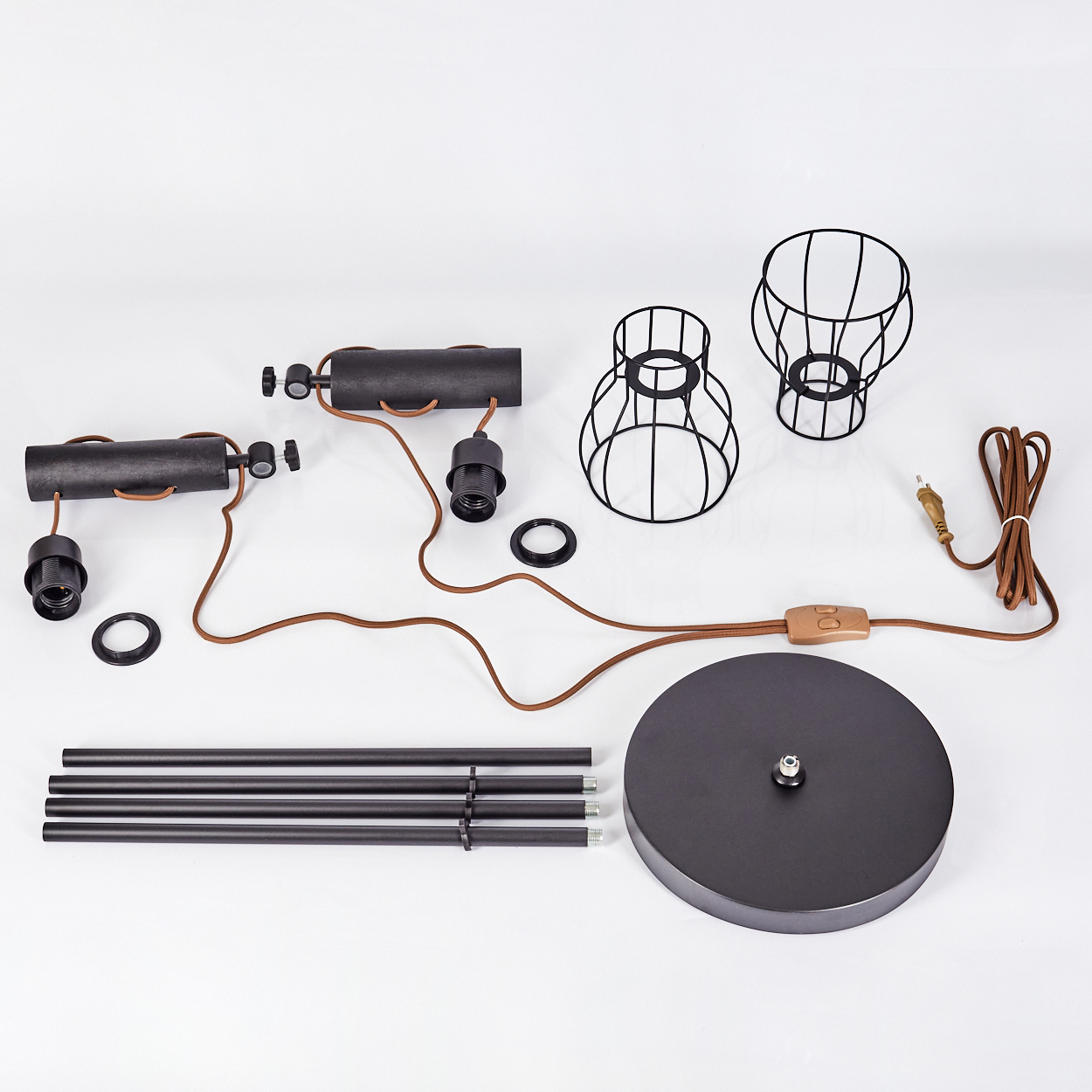 Zerlegte schwarze Metall-Stehlampe. Enthält Sockel, Stangen, Drahtkäfige, Lampenfassungen und Kabel. Teile sind auf weißem Untergrund angeordnet.