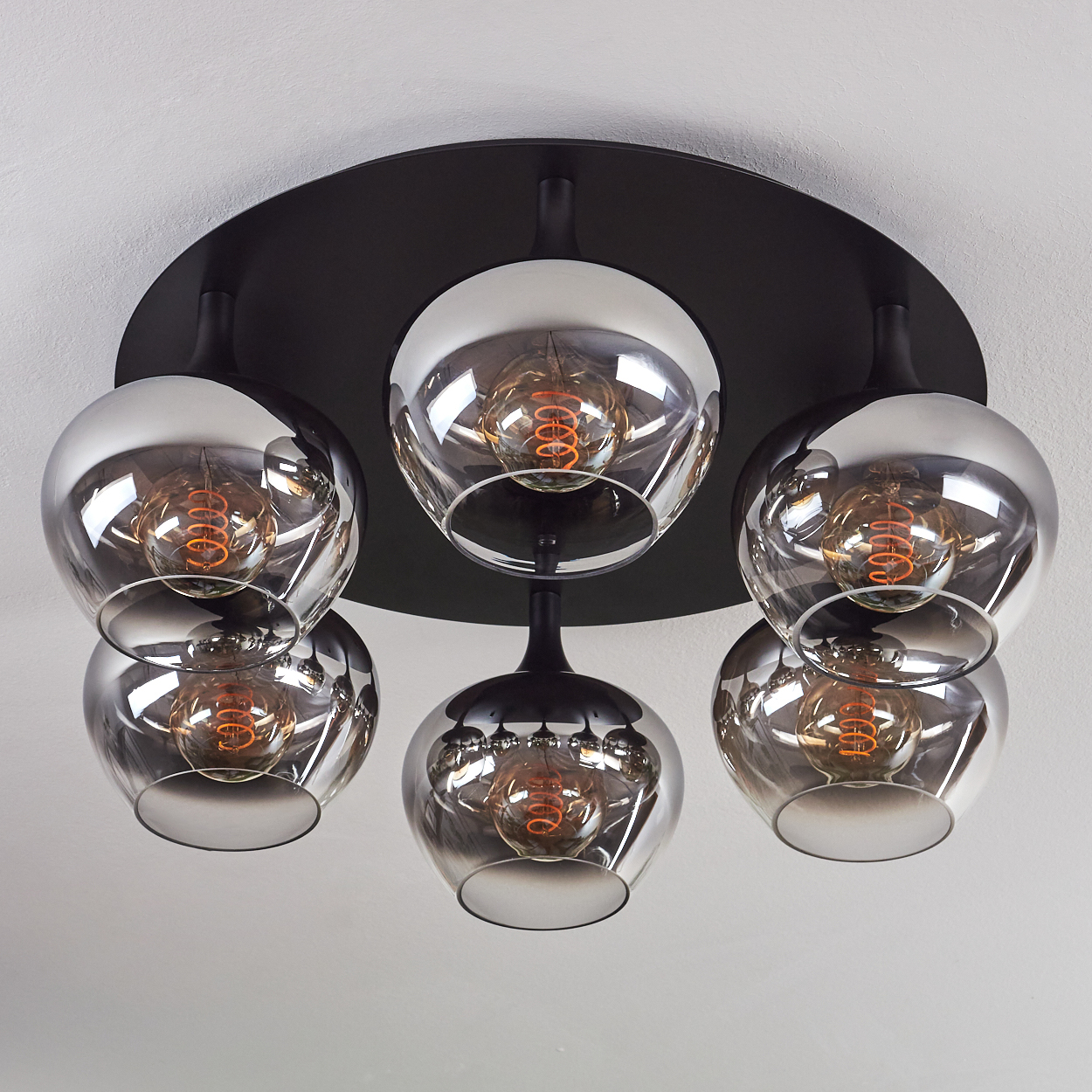 Eine moderne Deckenlampe mit sechs kugelförmigen Glasschirmen. Jeder Schirm hat eine sichtbare Glühbirne mit Wendel.