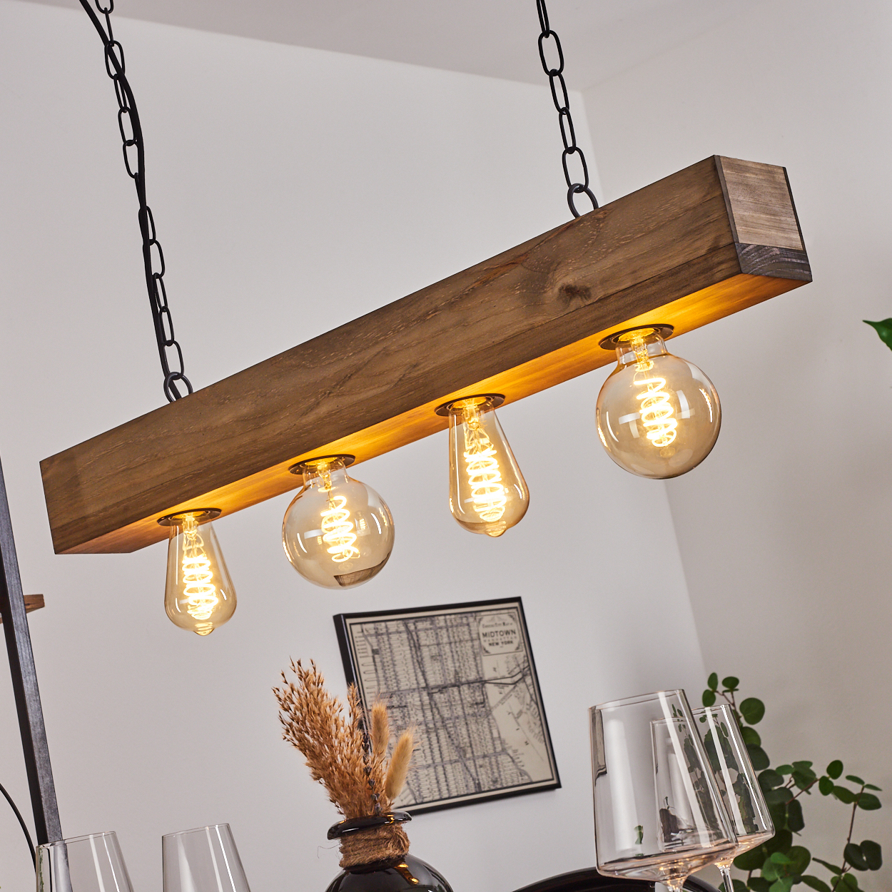 Eine Holzbalken-Leuchte mit vier Edison-Glühbirnen hängt an Ketten. Der Hintergrund umfasst eine Karte, eine Vase und Gläser.