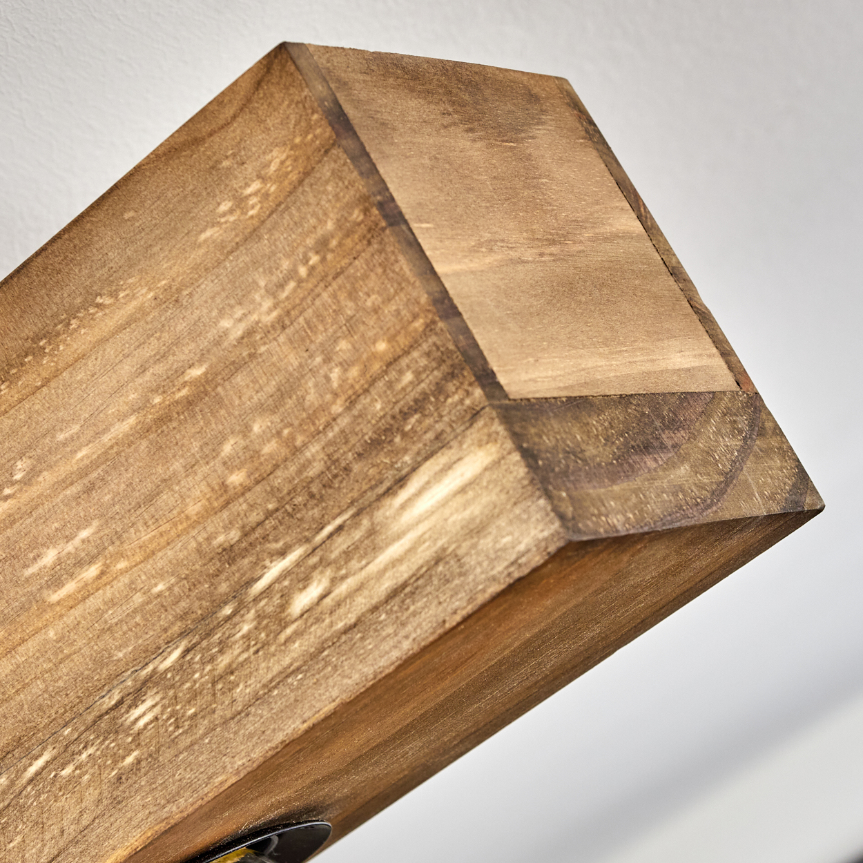 Nahaufnahme eines Holzbalkens mit sichtbarer Maserung und dunkler Beize. Der Balken ist vor weißem Hintergrund abgewinkelt.