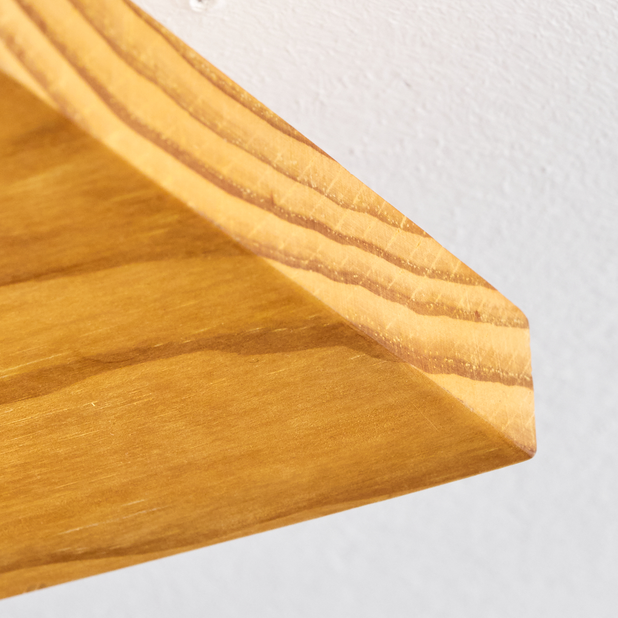 Nahaufnahme einer hölzernen Regal-Ecke vor einer weißen Wand. Das Holz ist hellbraun mit sichtbarer Maserung. Die Wand ist glatt.