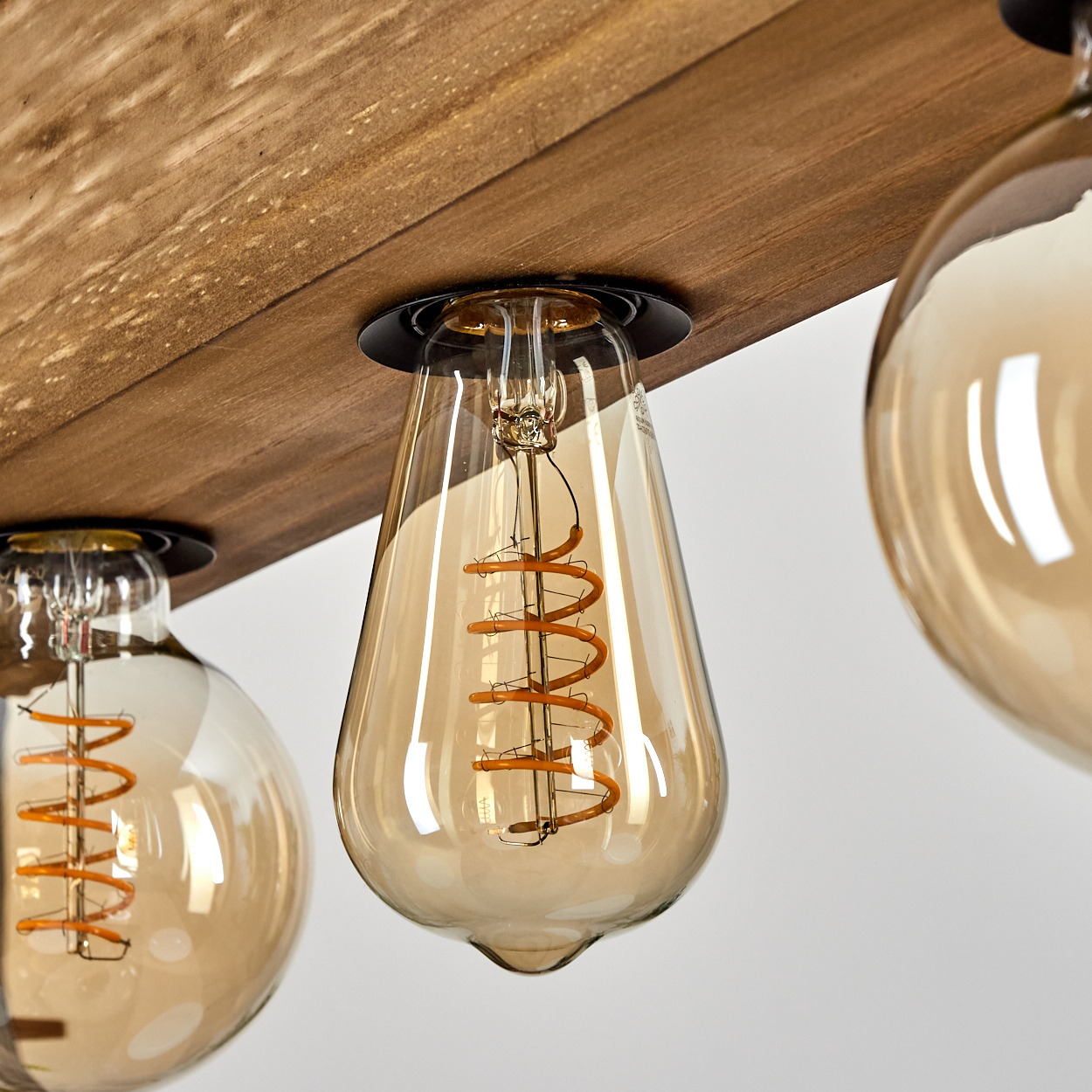 Nahaufnahme einer Leuchte mit drei Edison-Glühbirnen. Holzträger oben. Die Glühbirnen sind bernsteinfarben und haben Spiralfäden.