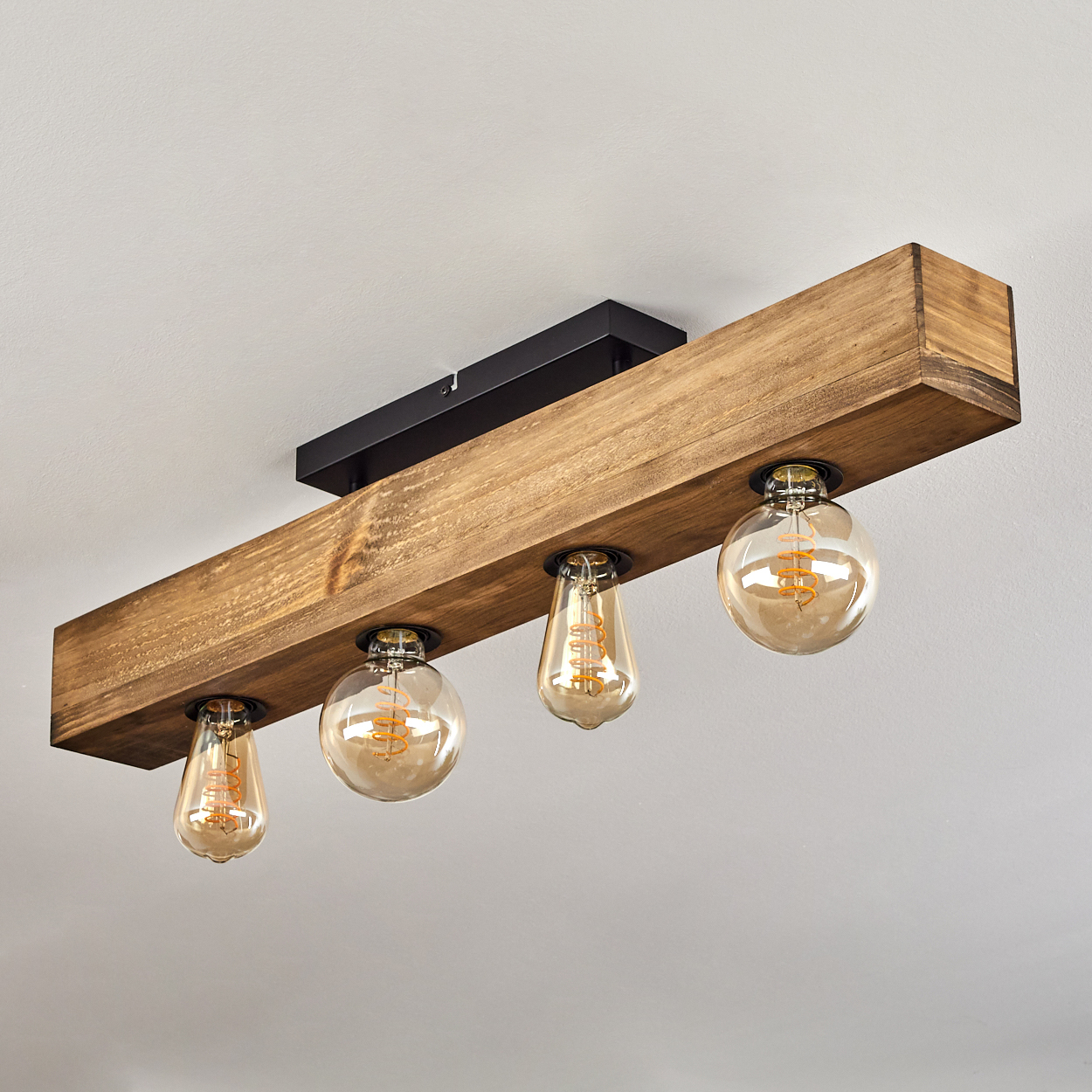Eine Deckenleuchte aus Holzbalken mit vier warm getönten Glühbirnen. Der Balken ist braun, die Leuchte an einer weißen Decke montiert.