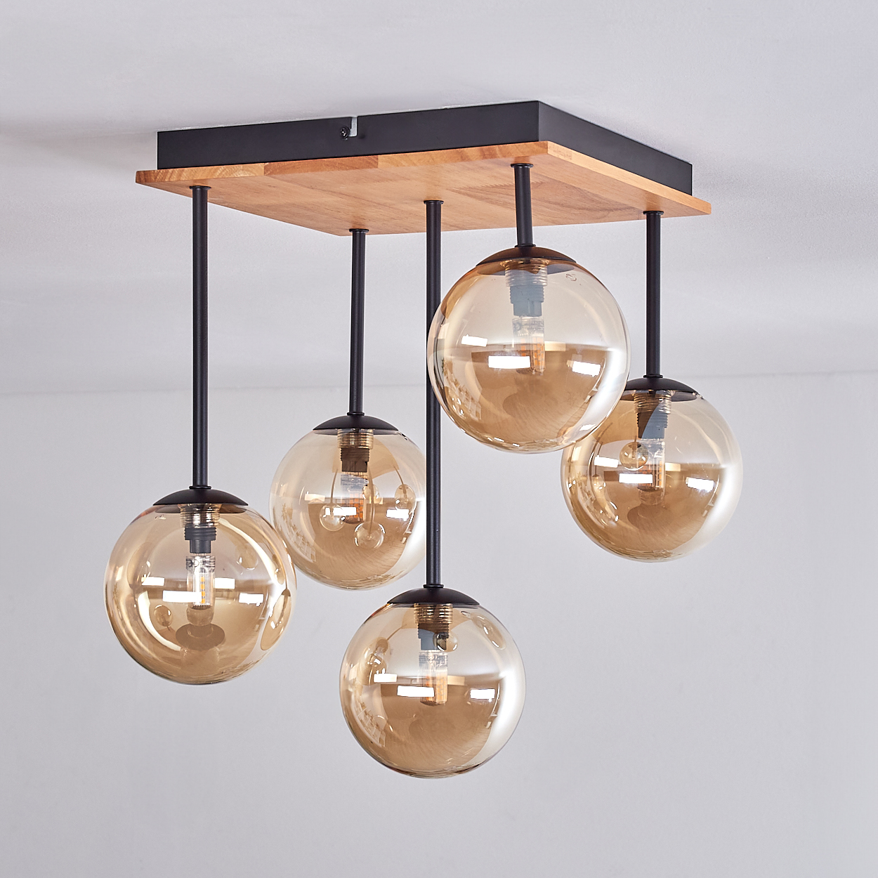 Eine Deckenleuchte mit fünf bernsteinfarbenen Glaskugeln. Die Leuchte hat einen Holzsockel mit schwarzen Metallstangen und einem weißen Deckenhintergrund.