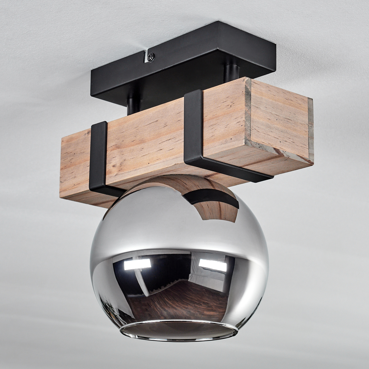 Eine moderne Deckenleuchte mit einer Chromkugel, die unter einem Holzbalken hängt, der von schwarzen Metallhalterungen getragen wird.