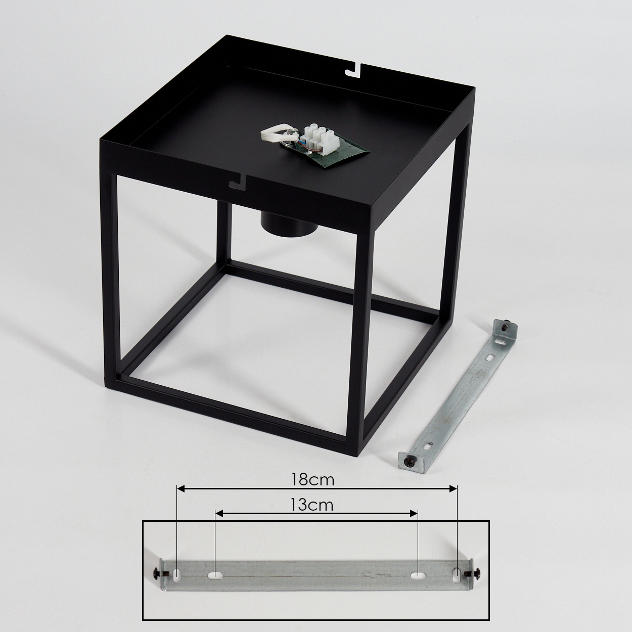 Schwarze quadratische Lampe mit Komponenten oben, einer Metallhalterung und den Maßen 18 cm und 13 cm. Weißer Hintergrund.