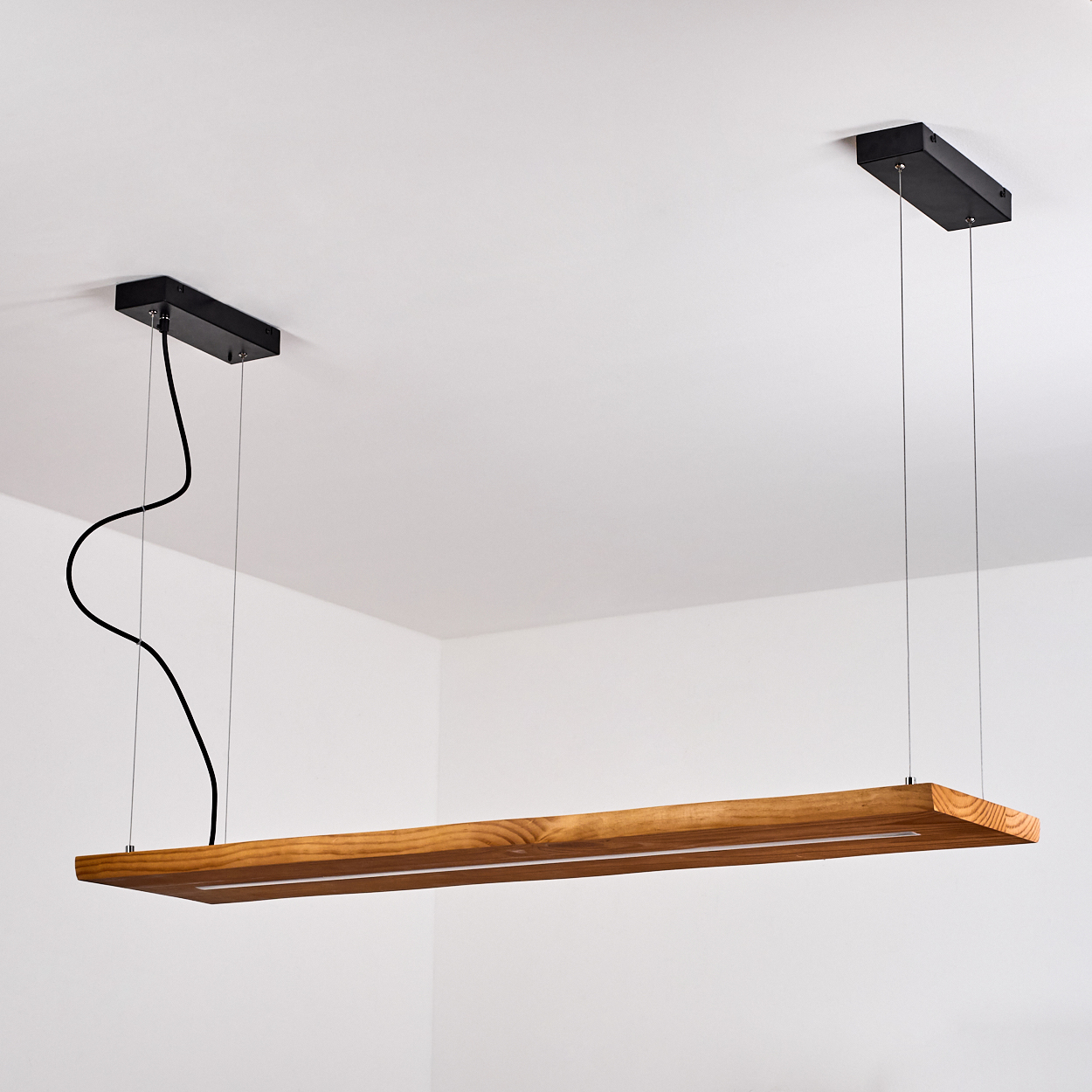 Eine rechteckige Holzleuchte hängt von der Decke. Schwarze Montagekästen und ein schwarzes Kabel sind sichtbar.
